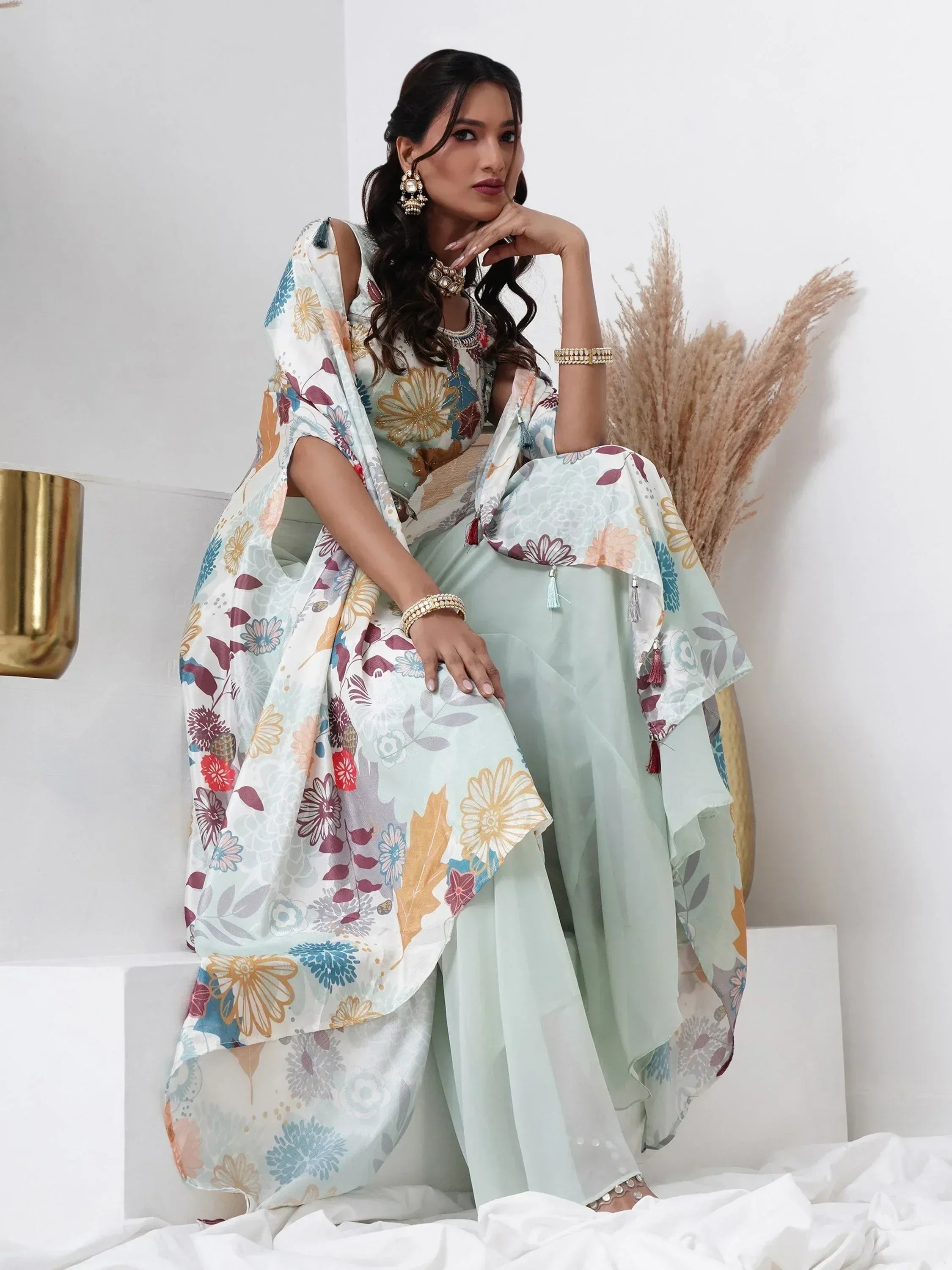 Woman in pastel floral printed ethnic saree set with statement jewelry, sitting indoors