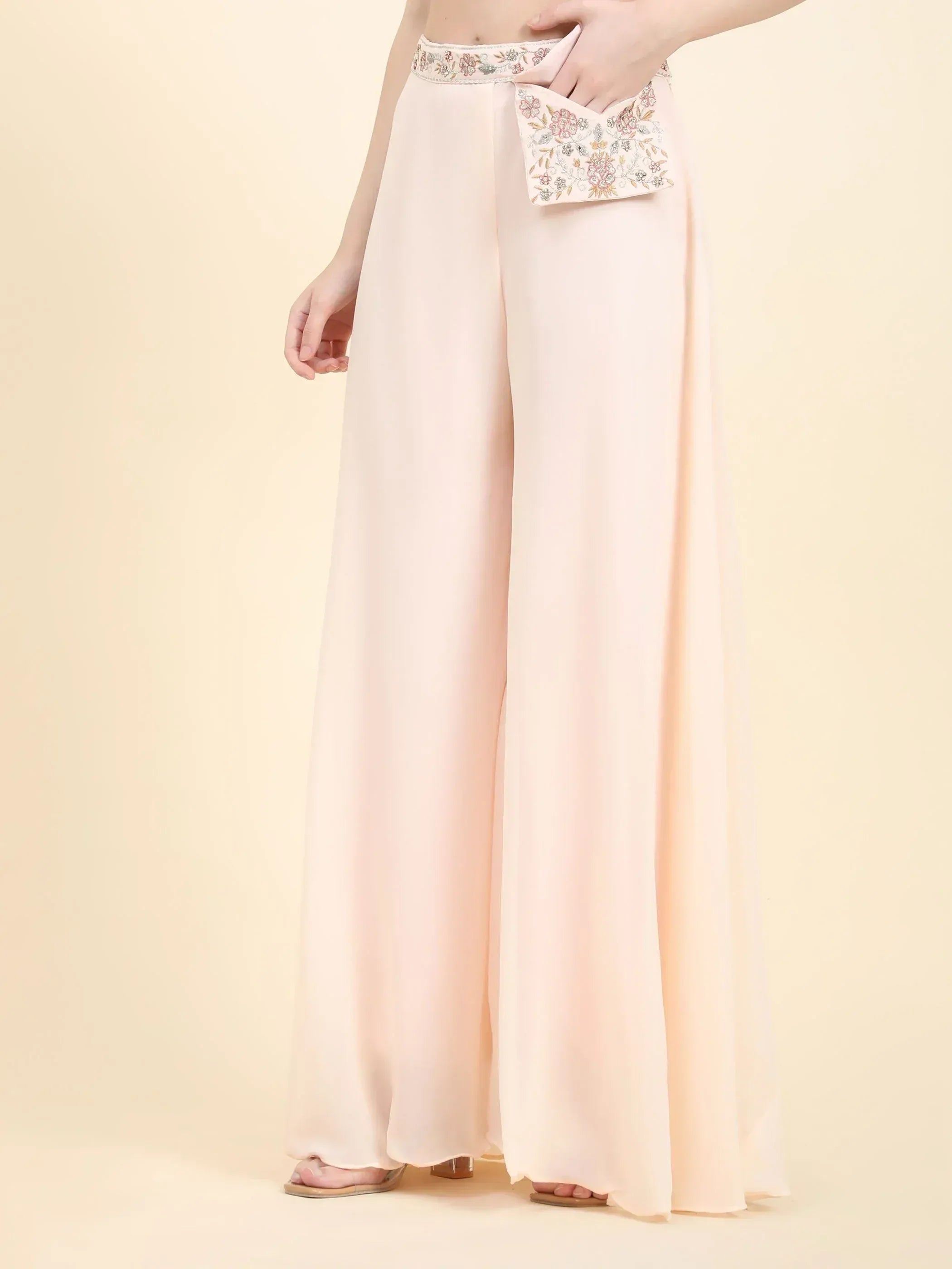 Woman wearing pastel peach palazzo pants with floral embroidered waistband and clutch