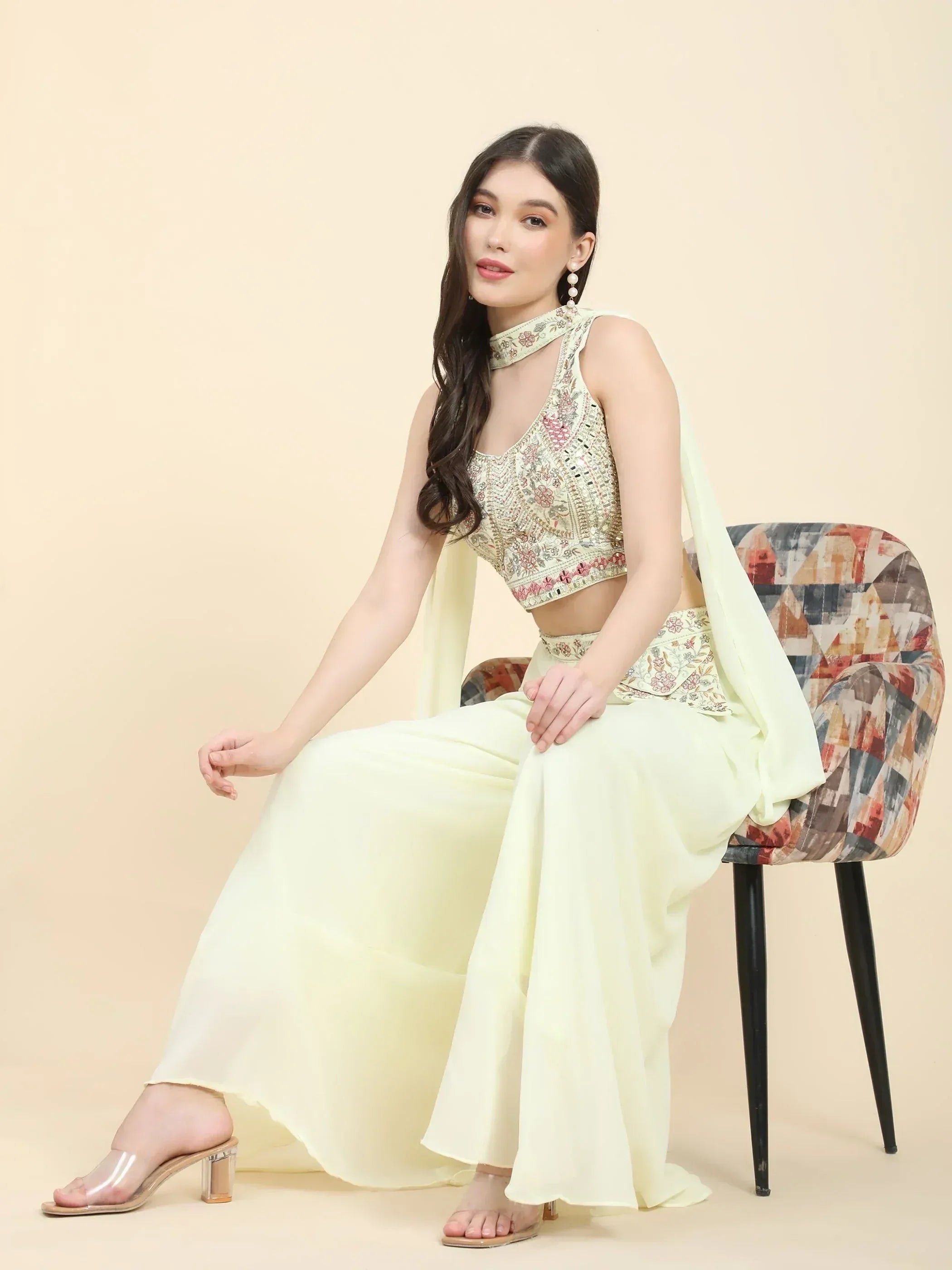 Woman in pastel embroidered lehenga choli with dupatta, seated on a chair, ethnic wear