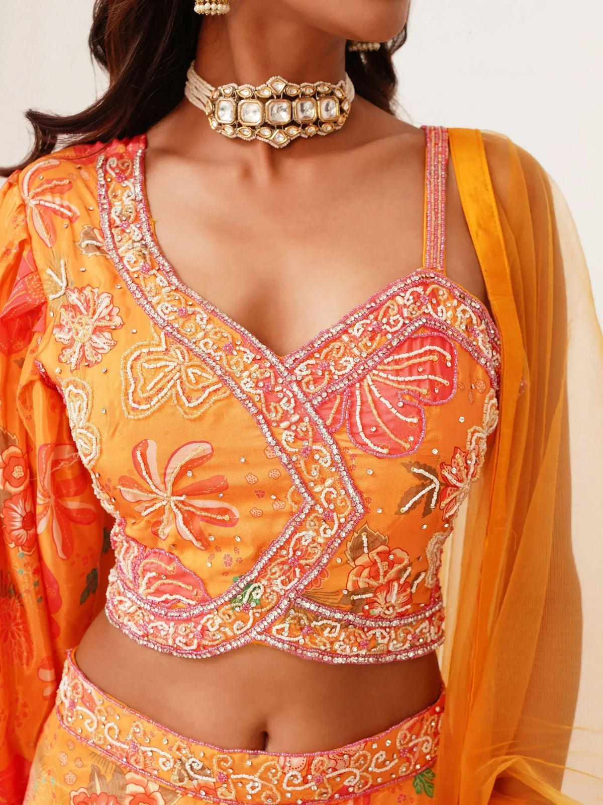 Orange floral embroidered lehenga choli with pink beadwork and V-neck blouse, paired with statement choker.