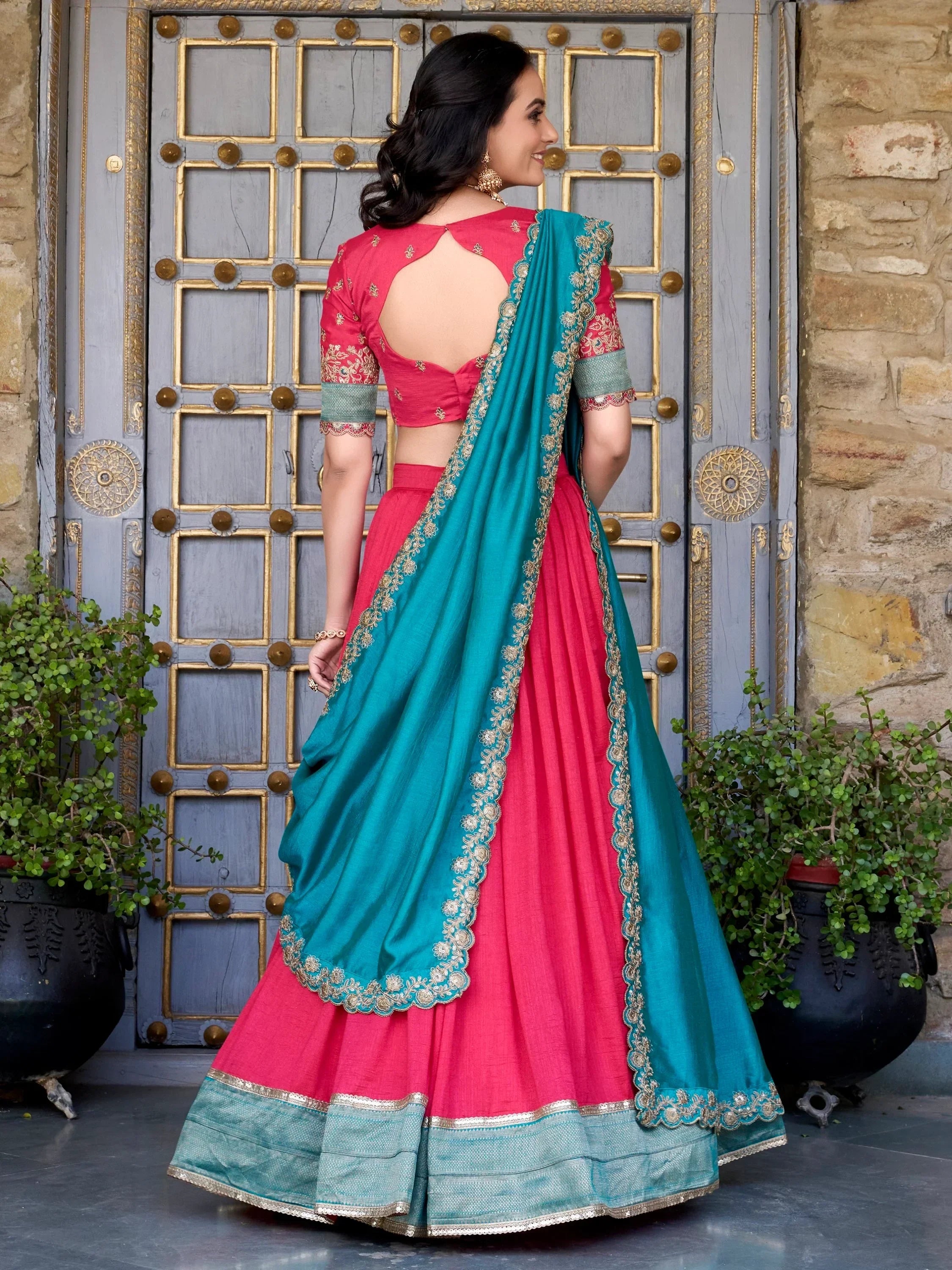 Pink and teal designer lehenga choli with gold embroidery, back view against ornate door