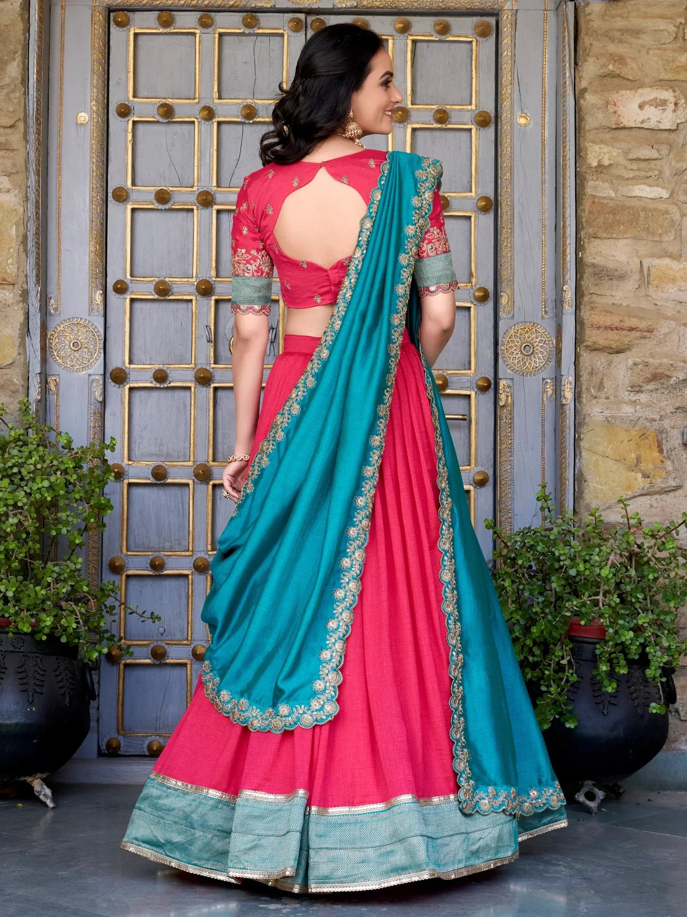 Pink and teal designer lehenga choli with gold embroidery, back view against ornate door