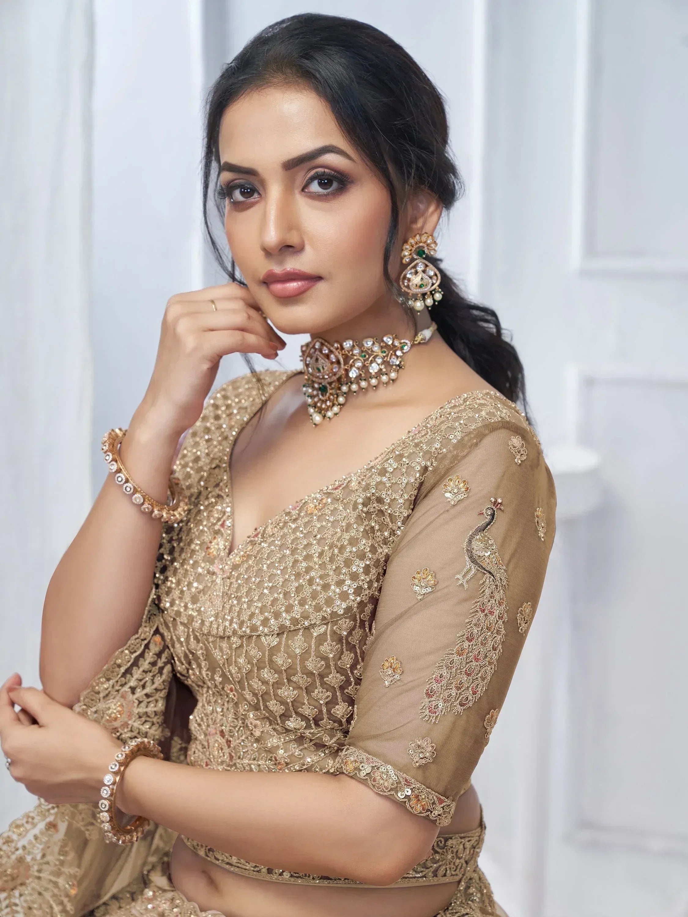 Elegant gold embroidered lehenga choli with peacock motif, paired with traditional Indian jewelry for festive occasions.