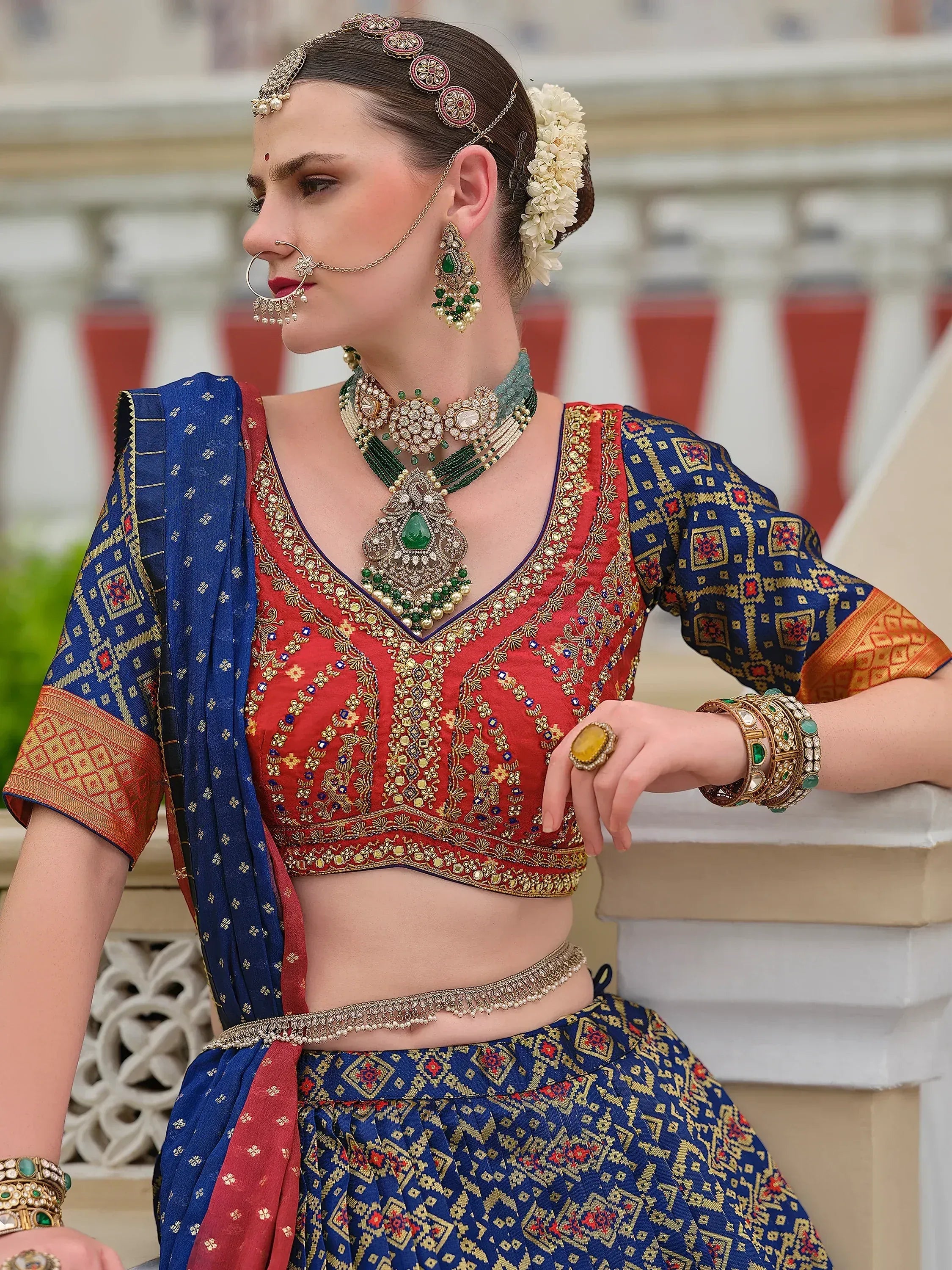 Woman in red and blue embroidered lehenga choli with traditional Indian jewelry and floral hair accessory