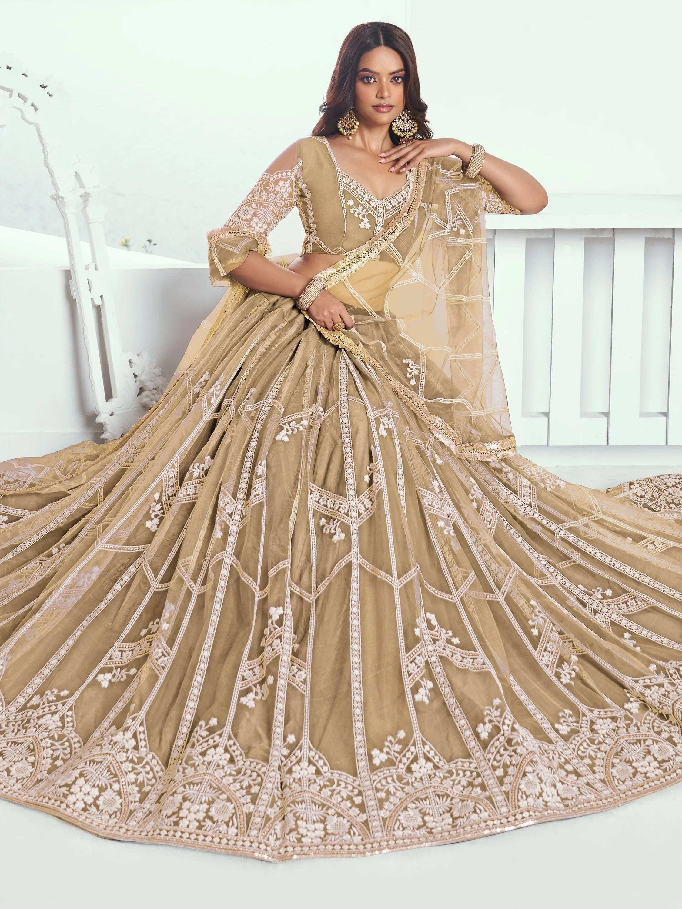 Beige designer lehenga choli with intricate white embroidery and sheer dupatta, perfect for Indian weddings.