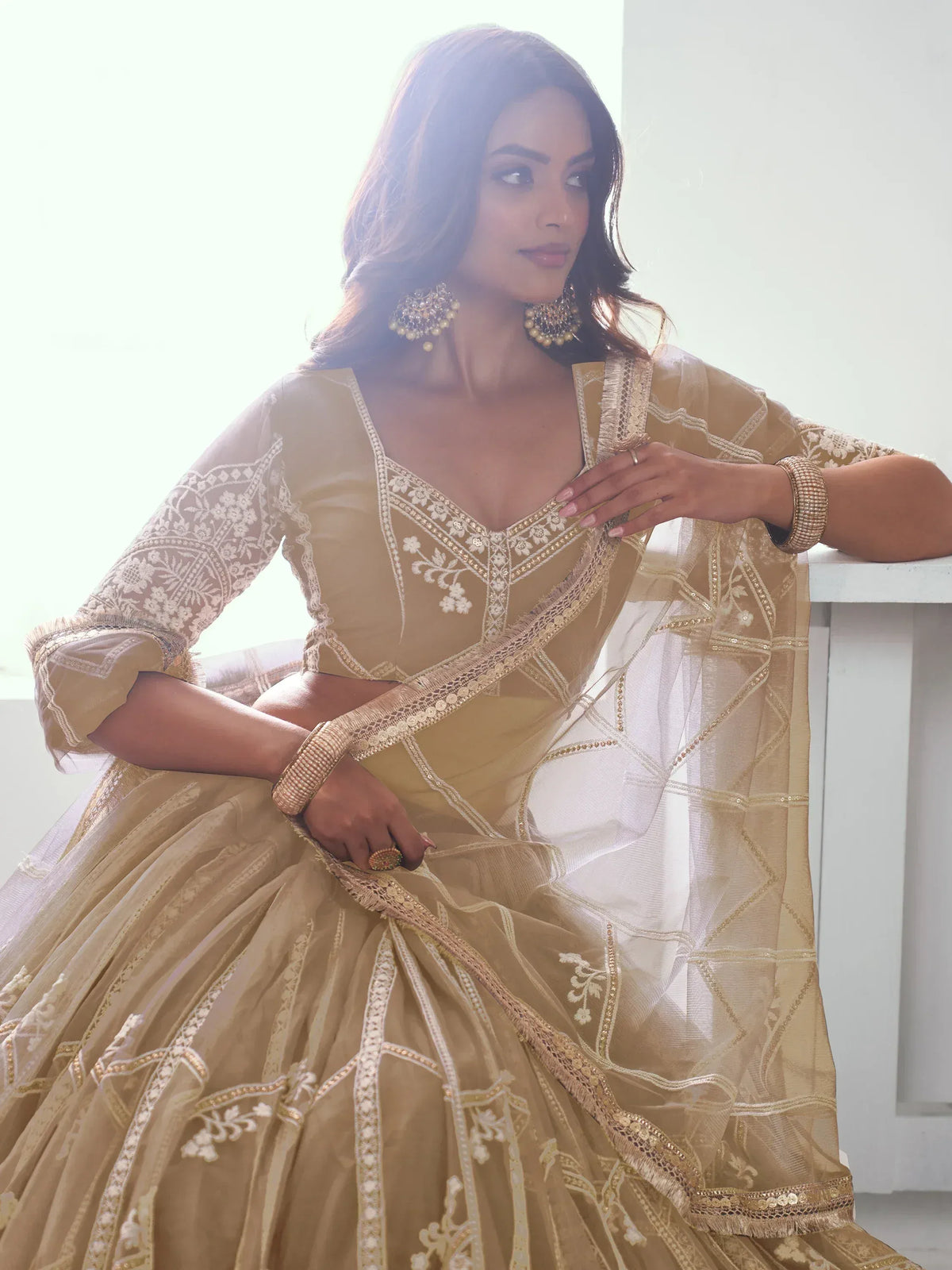 Elegant beige designer lehenga choli with intricate white embroidery and gold detailing, perfect for Indian ethnic occasions.