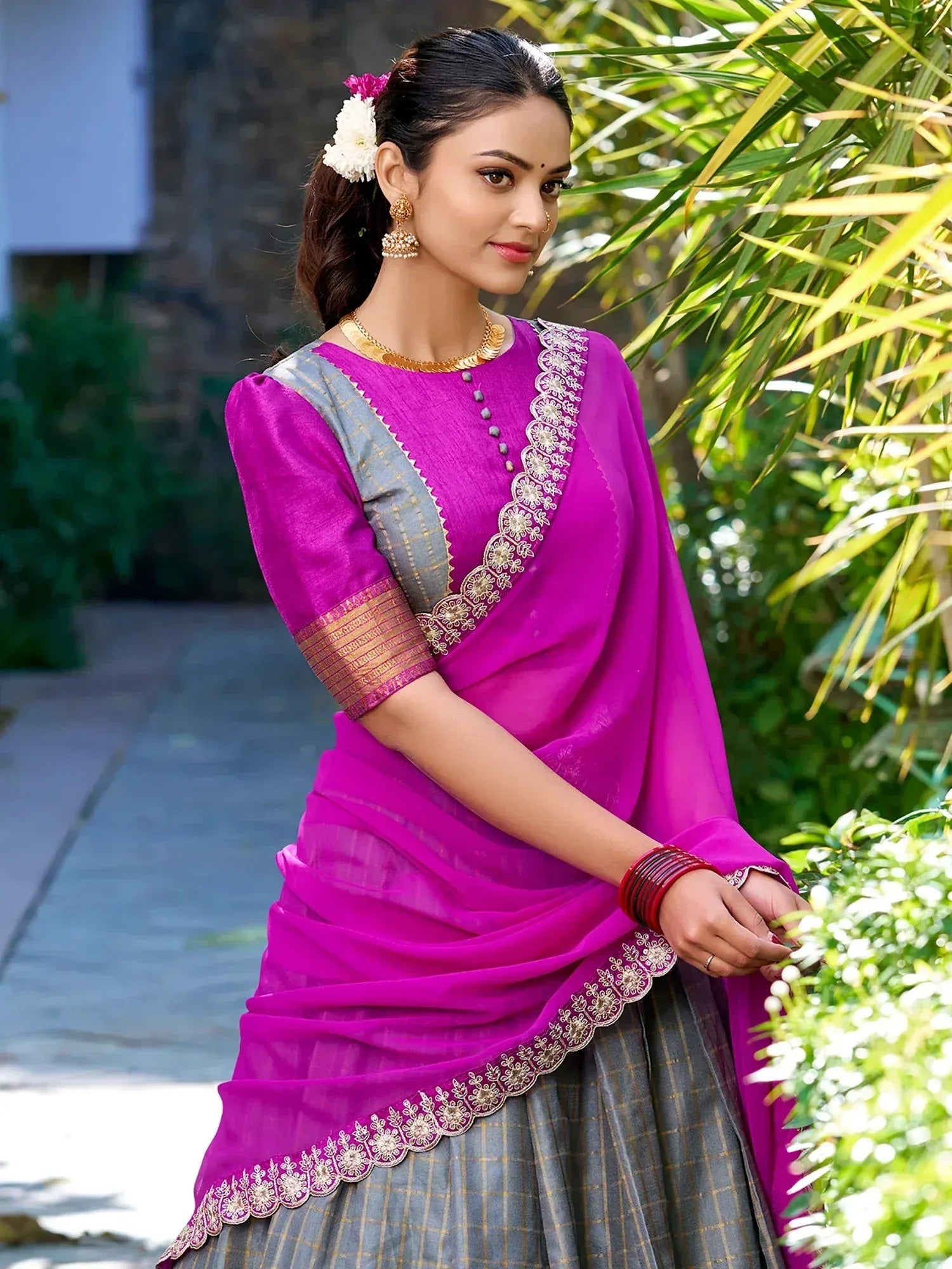 Vibrant magenta saree with gold embroidery and grey checkered blouse, styled with floral hair accessories and traditional jewelry.