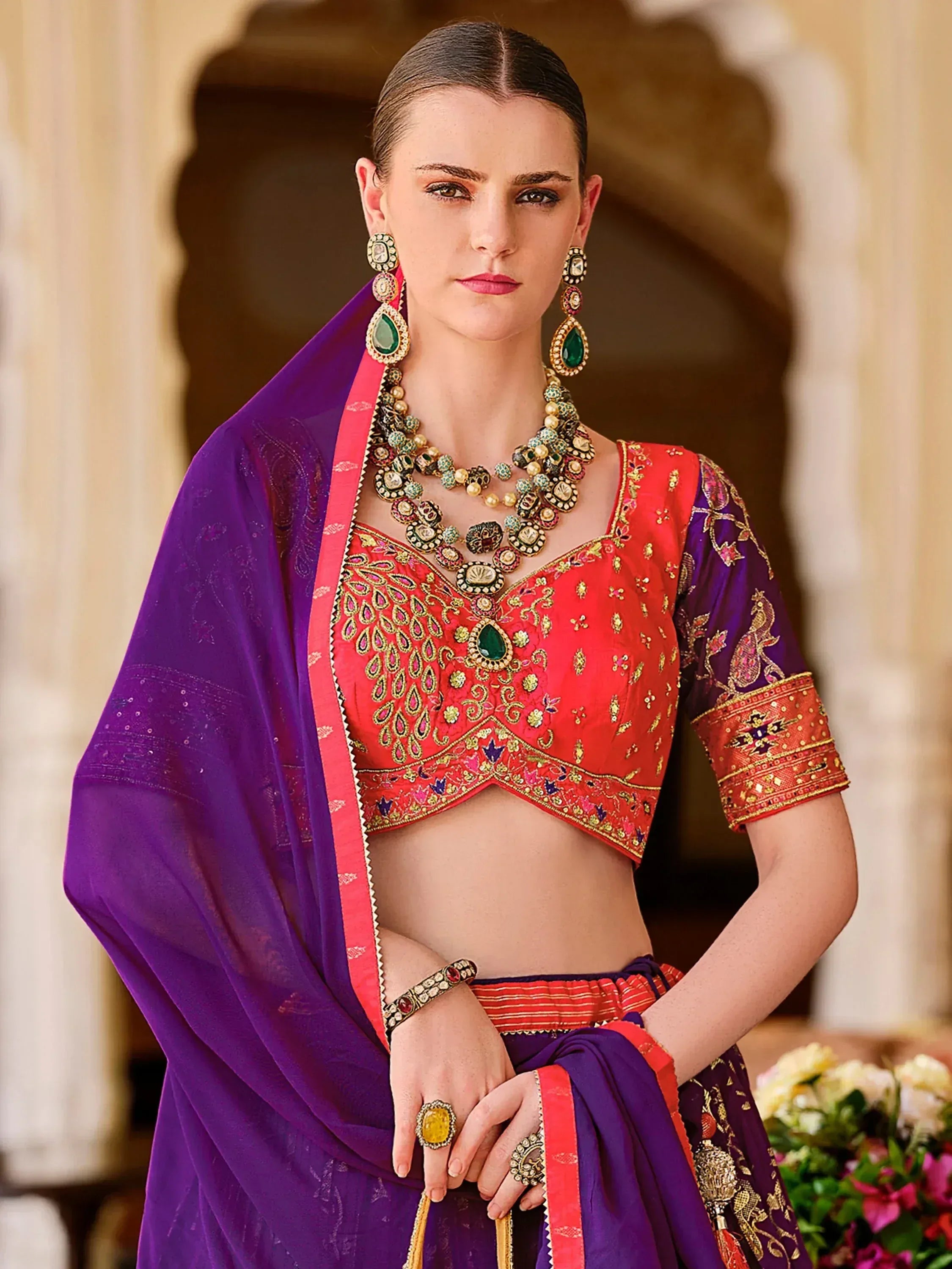 Red and purple embroidered Indian ethnic wear with heavy jewelry, perfect for festive occasions.