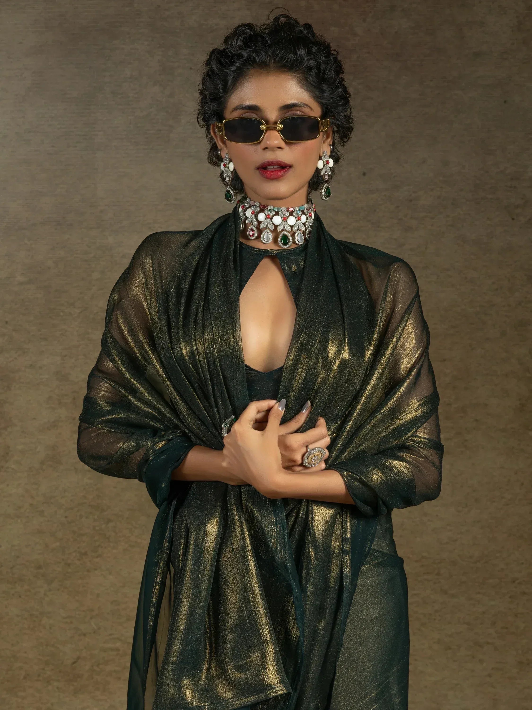 Elegant woman in emerald green ethnic gown with gold shimmer, statement jewelry, and sunglasses