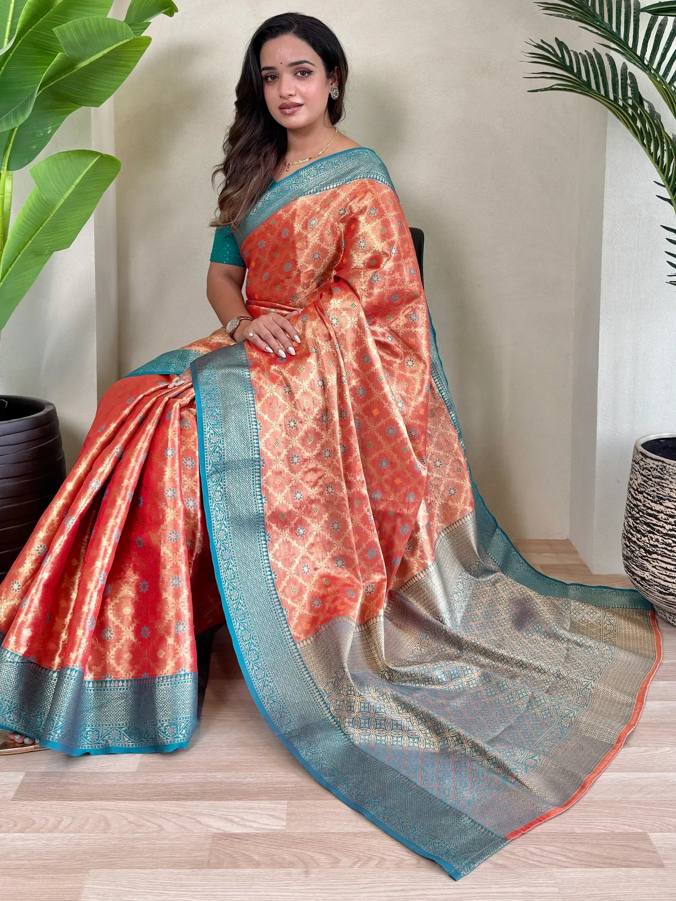 Woman in orange and teal designer saree with intricate gold patterns, perfect for Indian ethnic wear occasions.