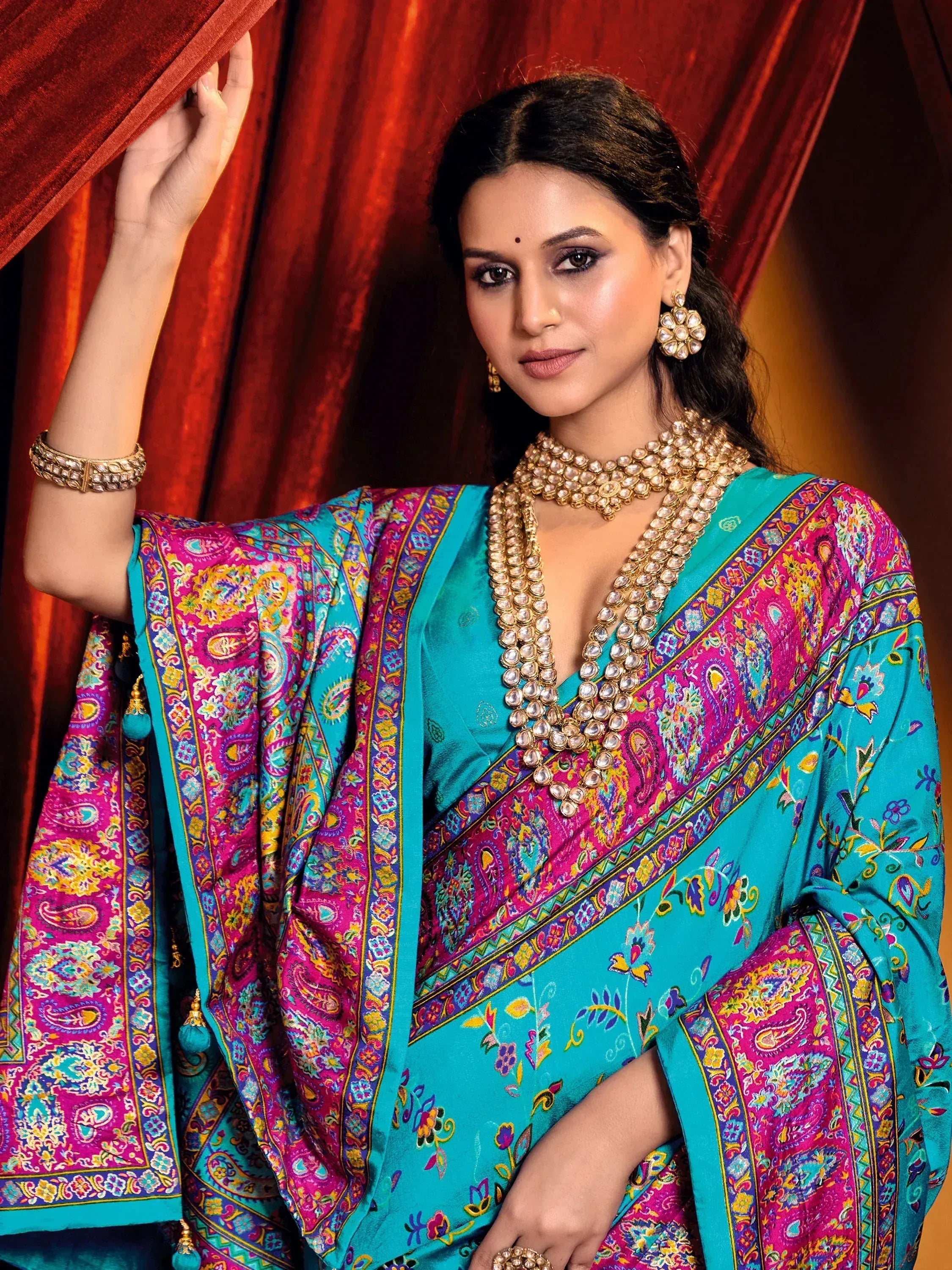 Woman in vibrant turquoise and pink paisley saree with gold jewelry, elegant ethnic wear