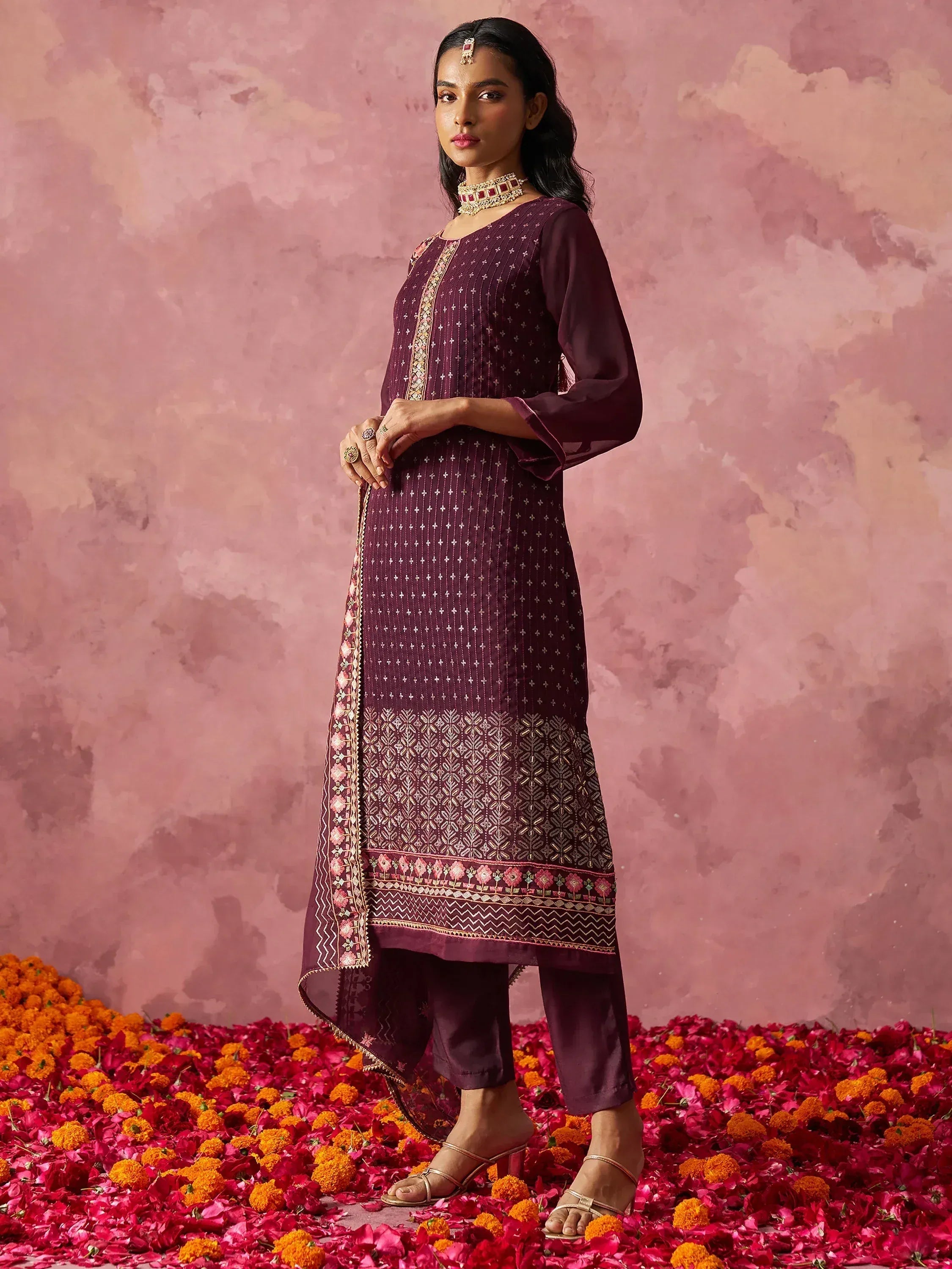 Elegant maroon ethnic kurta with gold embroidery, paired with matching pants, standing on floral petals.