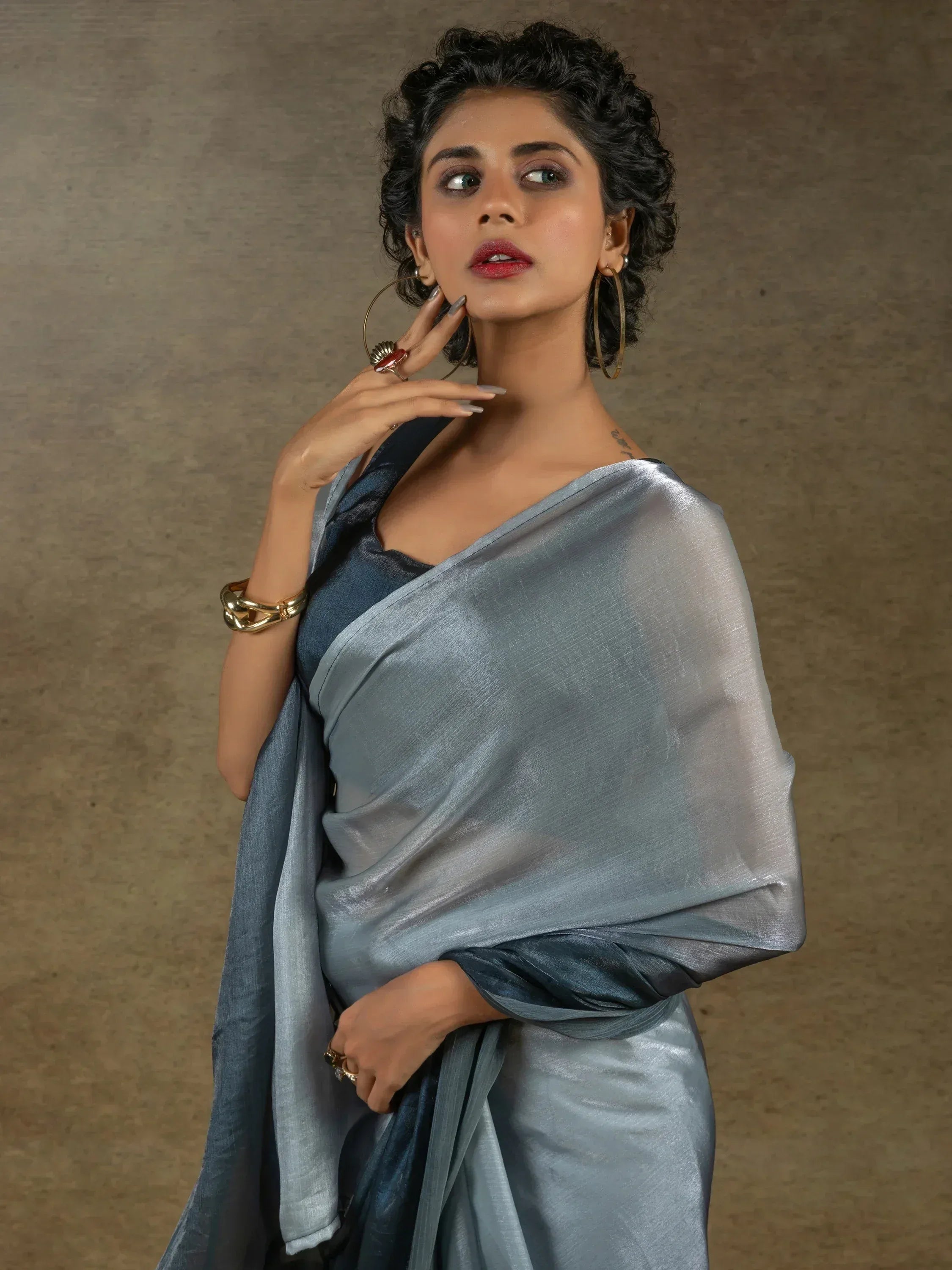Woman in elegant grey-blue saree with shimmer, styled with gold hoop earrings and statement rings
