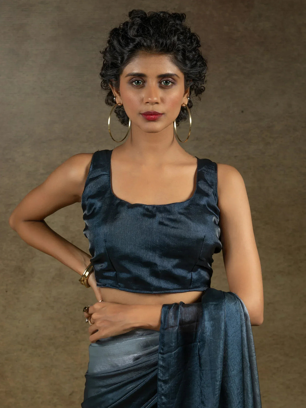 Woman in elegant navy blue satin saree with matching blouse, gold hoop earrings, and stylish curly updo.