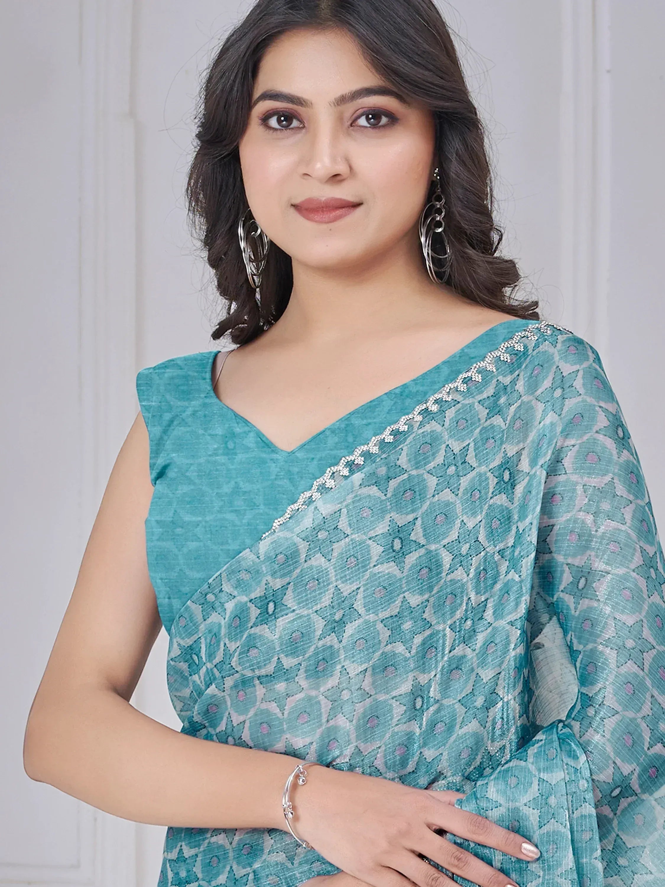 Teal printed saree with floral pattern and silver border, paired with sleeveless blouse for ethnic wear