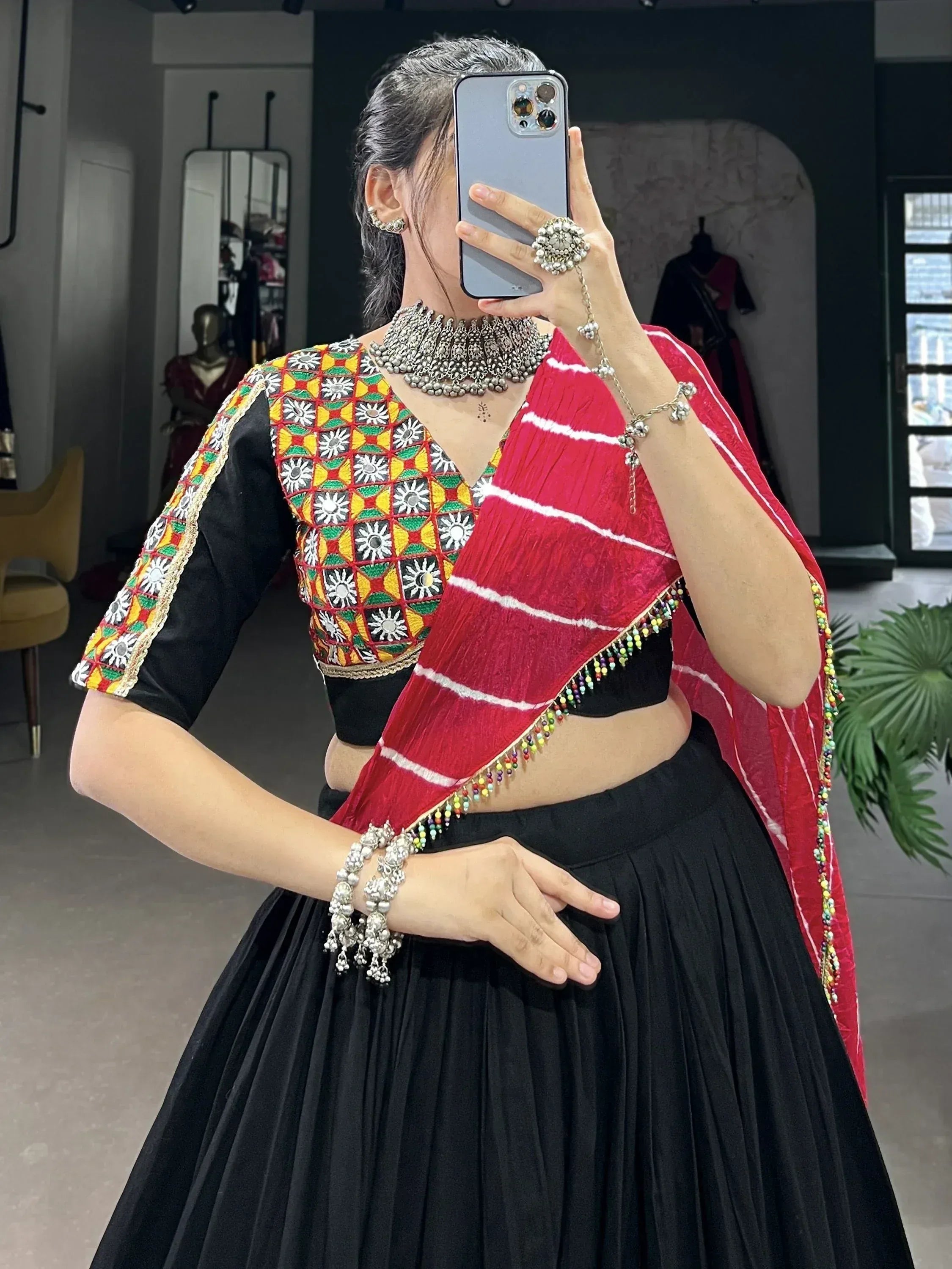 Woman in black lehenga with colorful embroidered blouse and red dupatta, styled with silver jewelry for Indian ethnic wear.