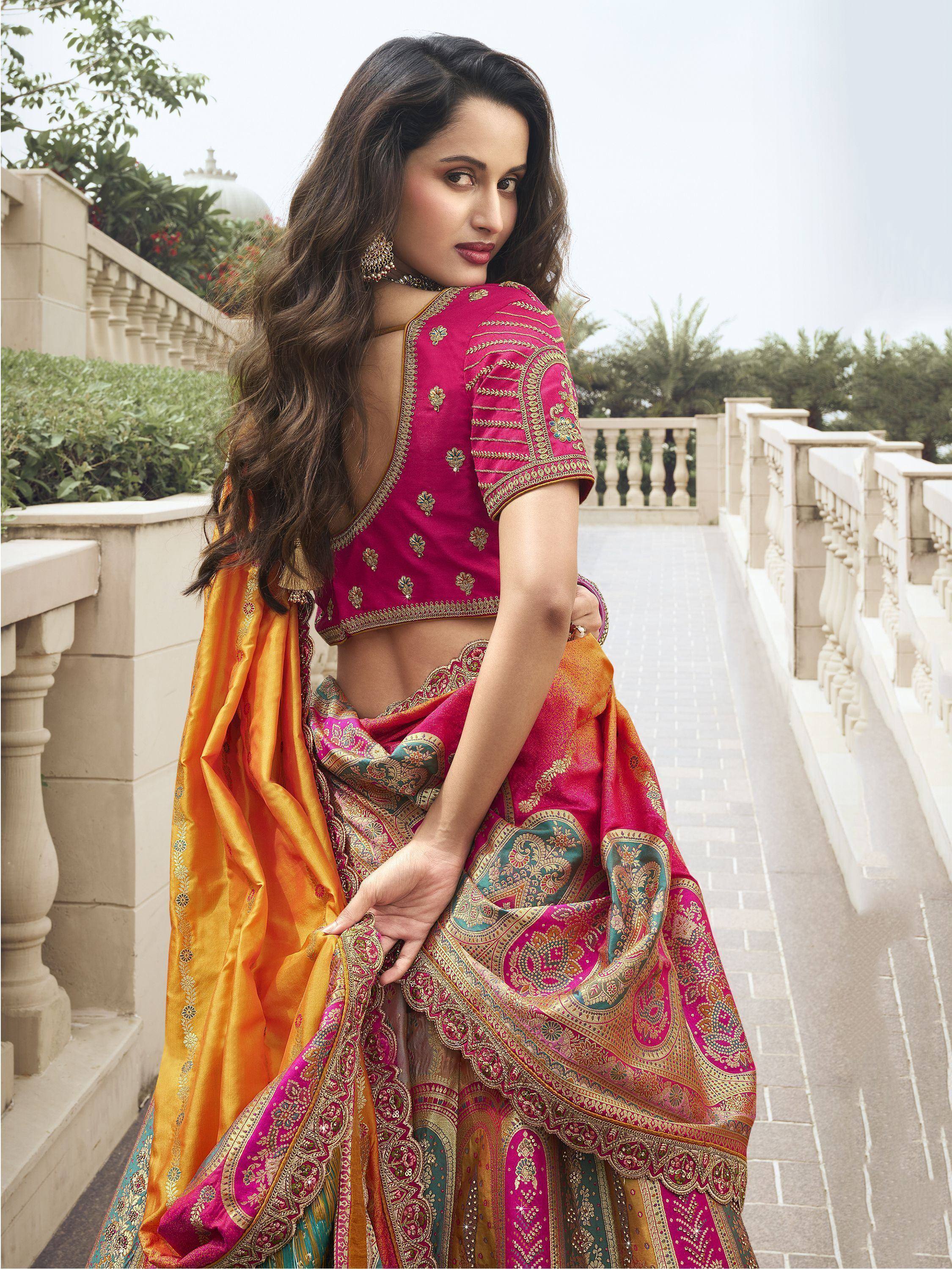 Woman in vibrant pink and orange designer lehenga choli with gold embroidery, perfect for Indian ethnic wear occasions.