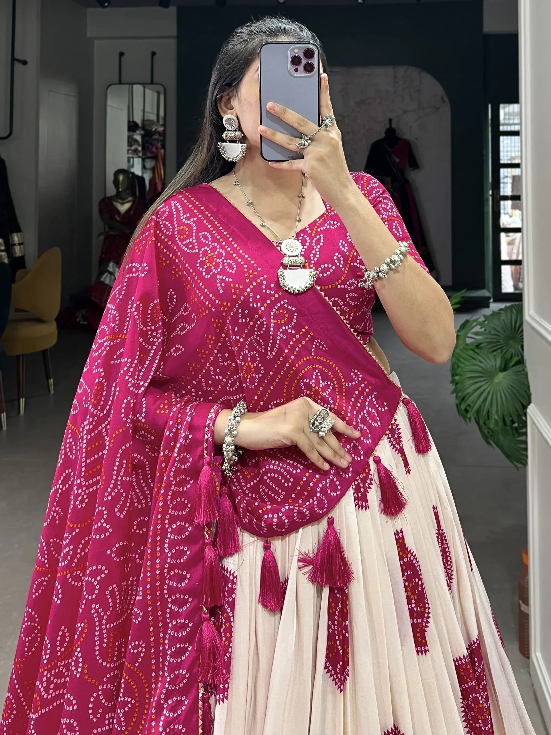 Woman in pink bandhani lehenga choli with tassels, mirror work jewelry, taking mirror selfie in boutique