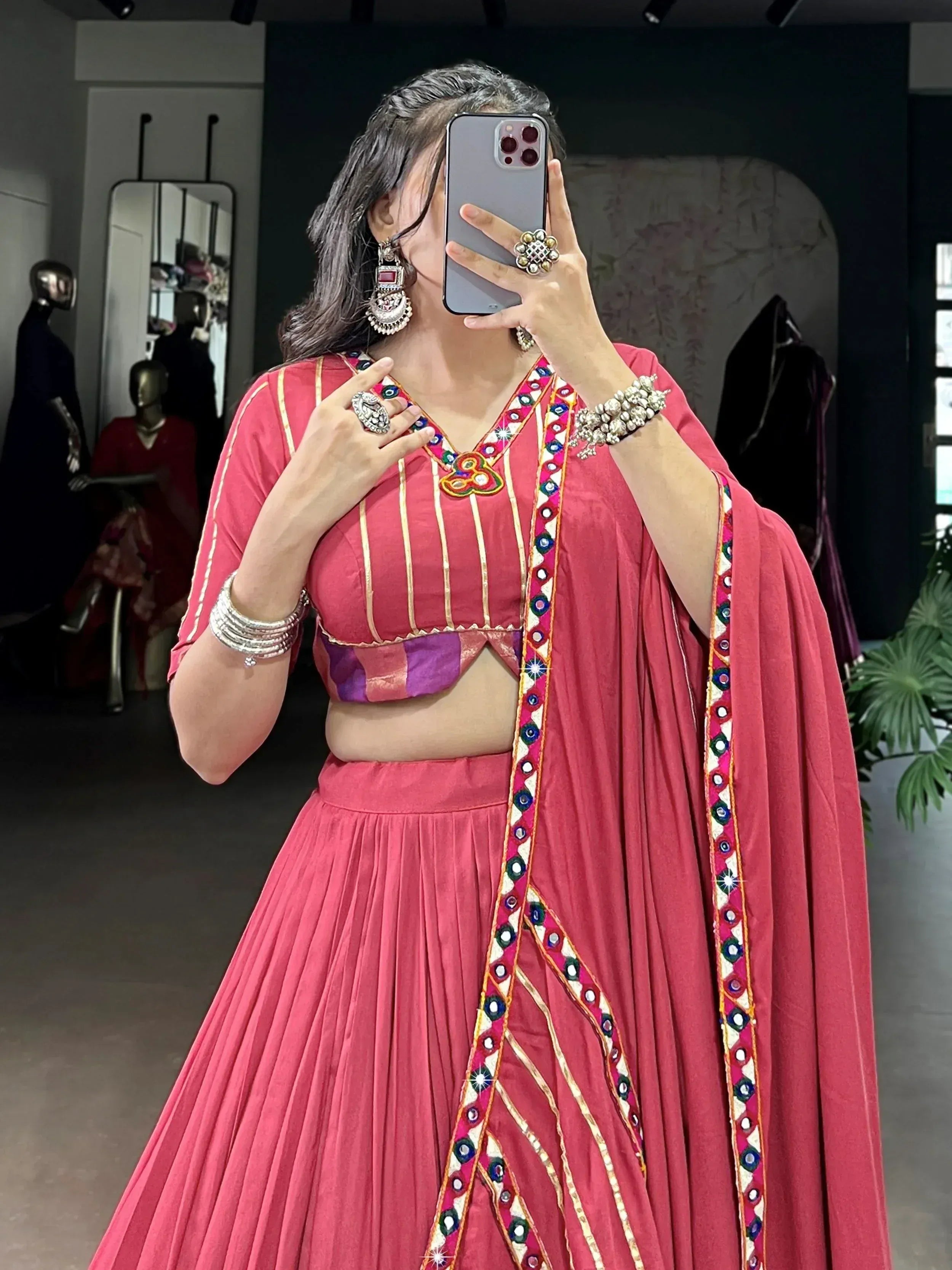 Pink ethnic lehenga choli with mirror work and gold trim, styled with traditional jewelry for festive occasions