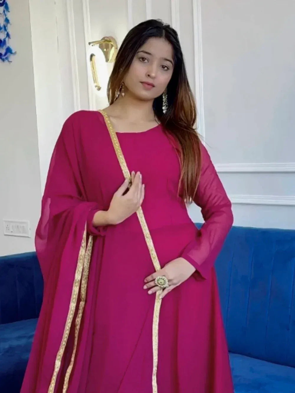 Magenta ethnic gown with gold trim, styled for Indian occasions, paired with statement jewelry