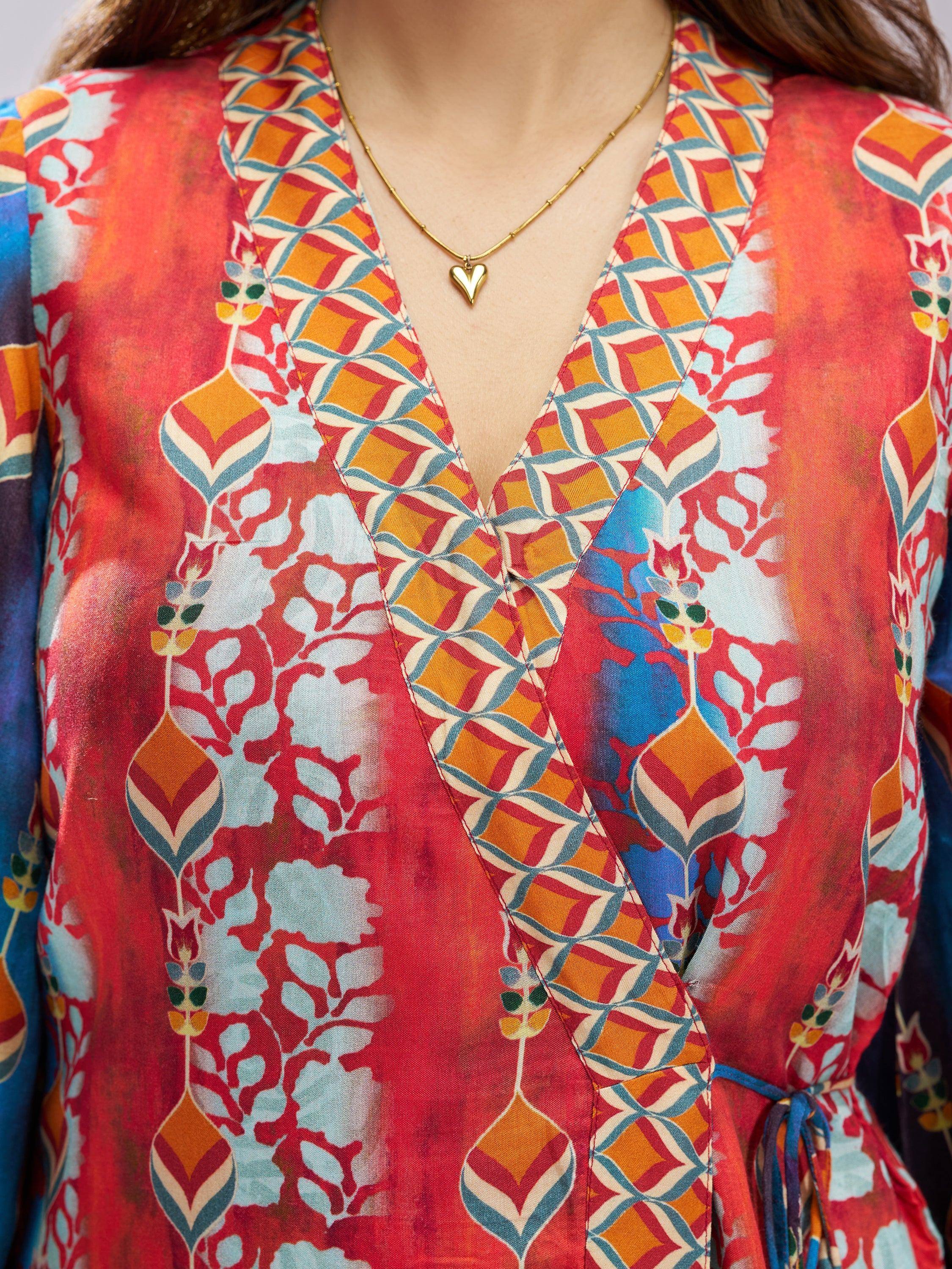 V-neck ethnic gown with vibrant red, blue, and orange geometric floral print, paired with gold heart necklace
