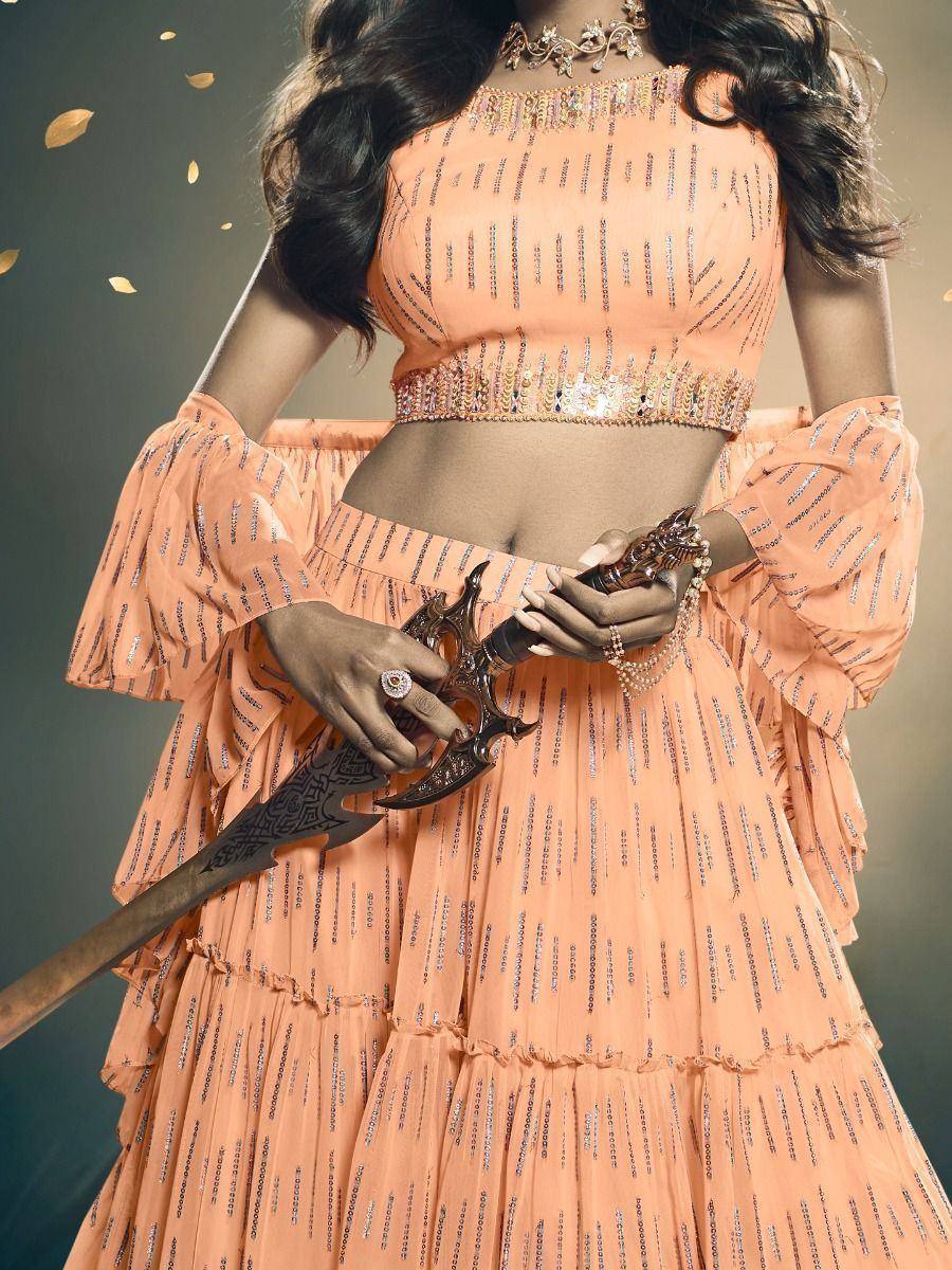 Peach designer lehenga choli with sequin detailing, ruffled sleeves, and ornate sword accessory for festive occasions