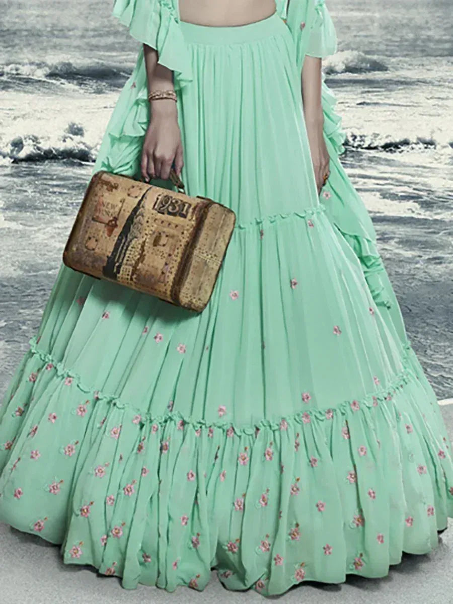 Mint green floral lehenga choli with ruffled sleeves, paired with vintage suitcase, beach backdrop
