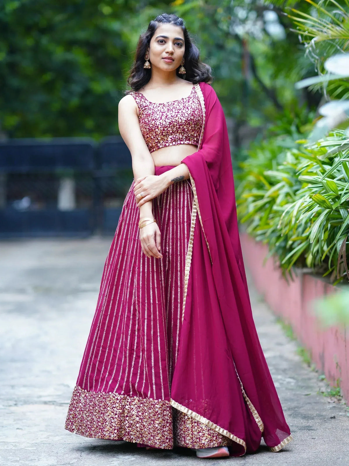 Woman in maroon designer lehenga choli with gold embroidery, perfect for Indian ethnic wear occasions.