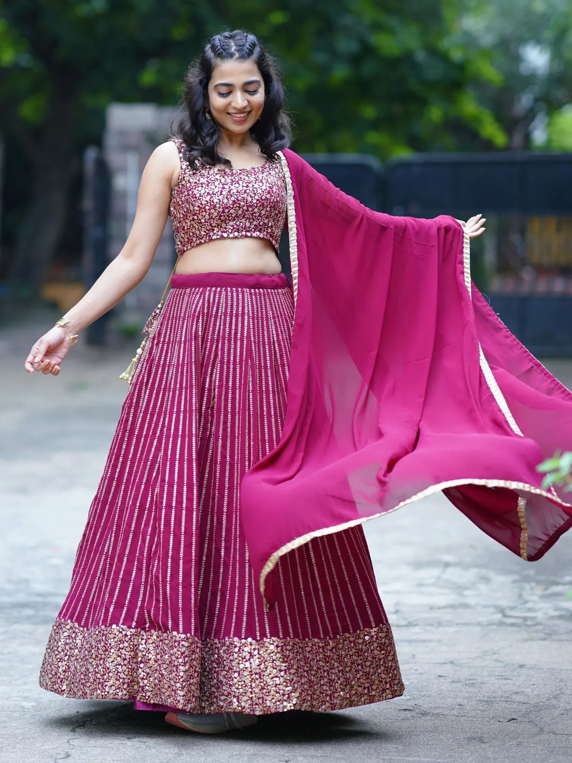Woman in maroon sequin lehenga choli with gold embroidery, twirling outdoors