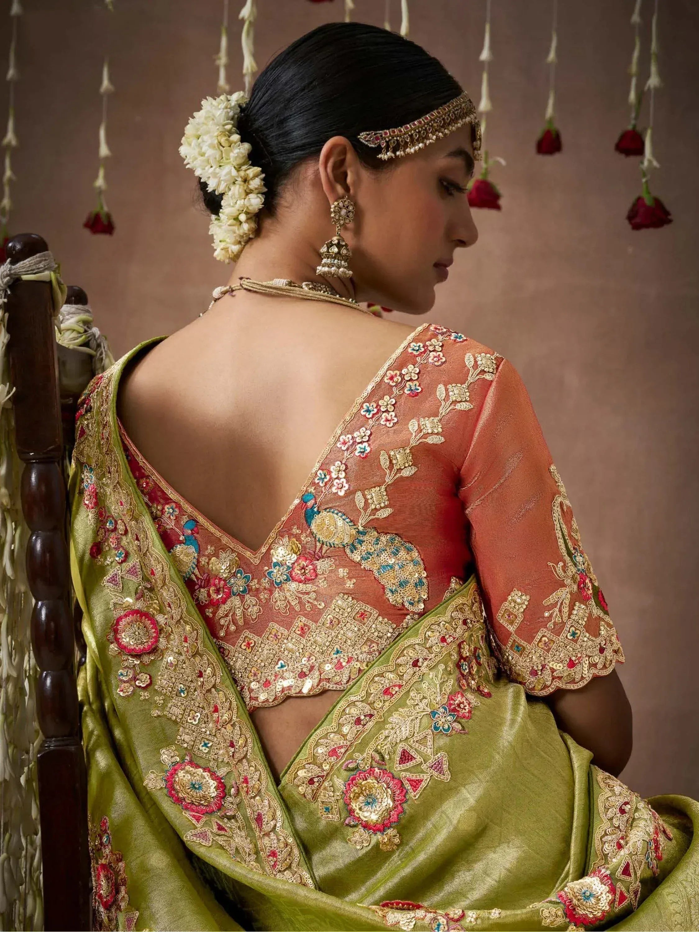 Woman in embroidered green saree with peach blouse, floral hair accessory, and traditional jewelry