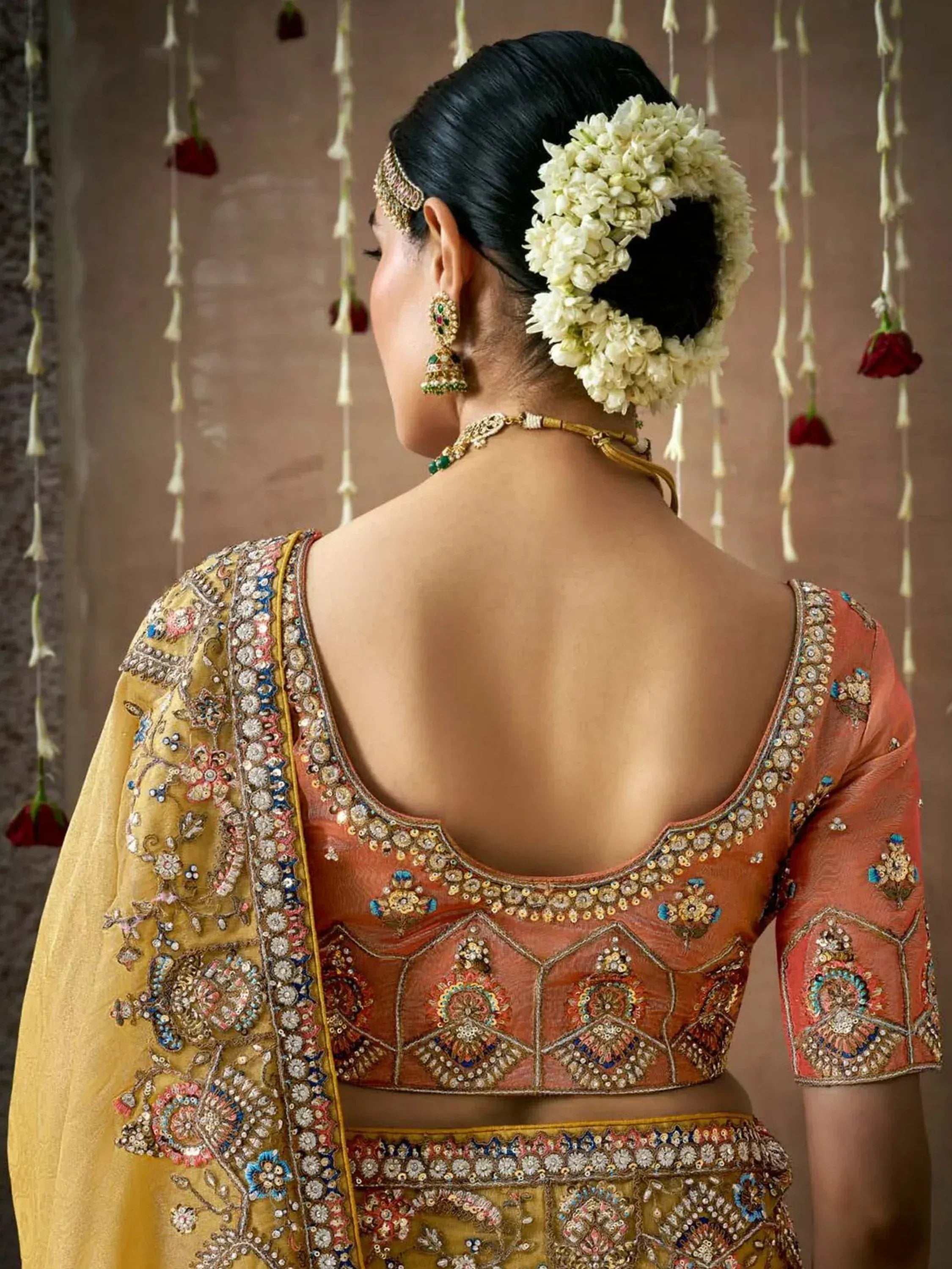 Back view of woman in embroidered peach and gold lehenga choli with floral hair accessory and traditional jewelry