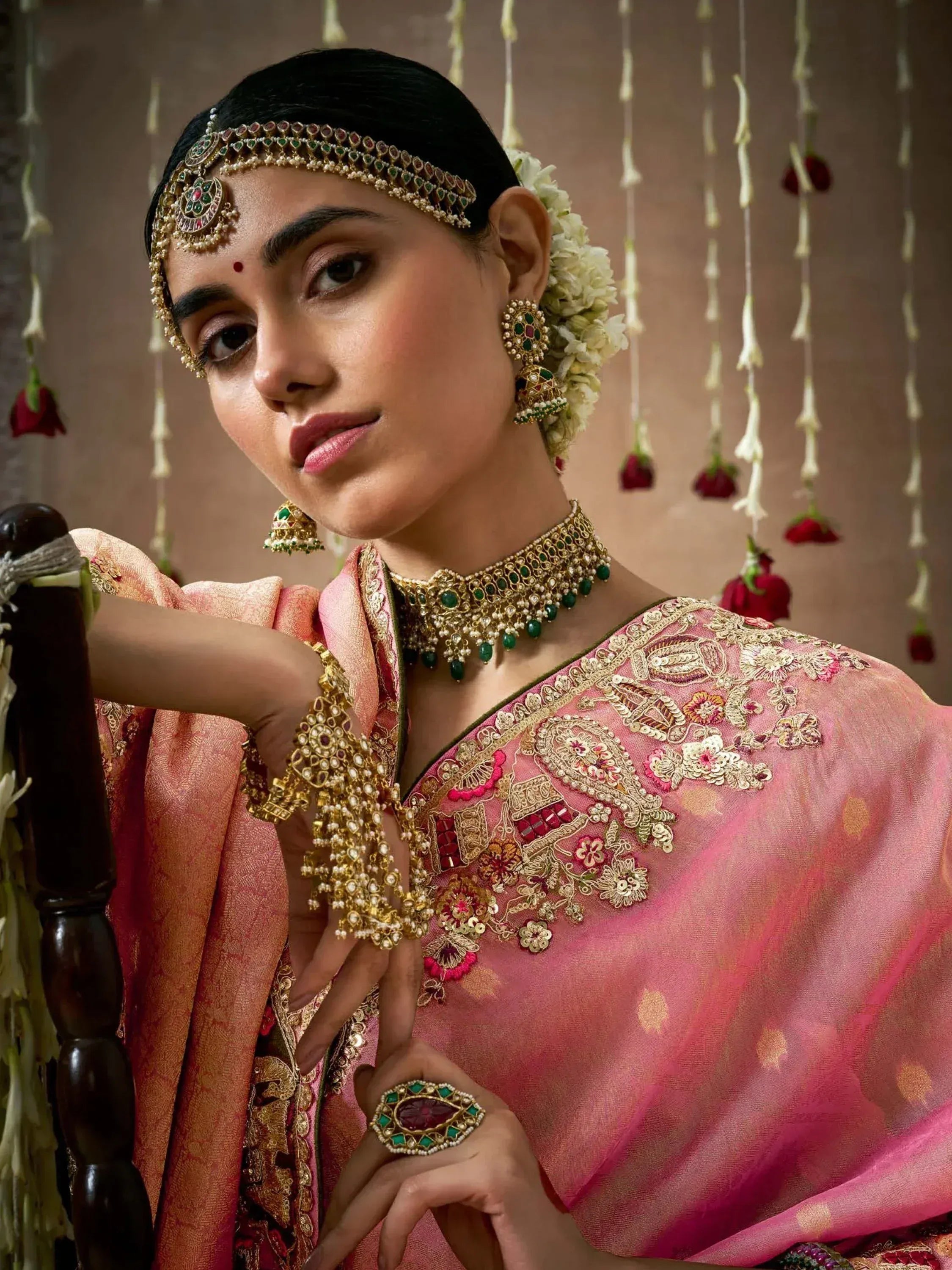 Elegant woman in pink embroidered saree with traditional Indian jewelry and floral hair accessories