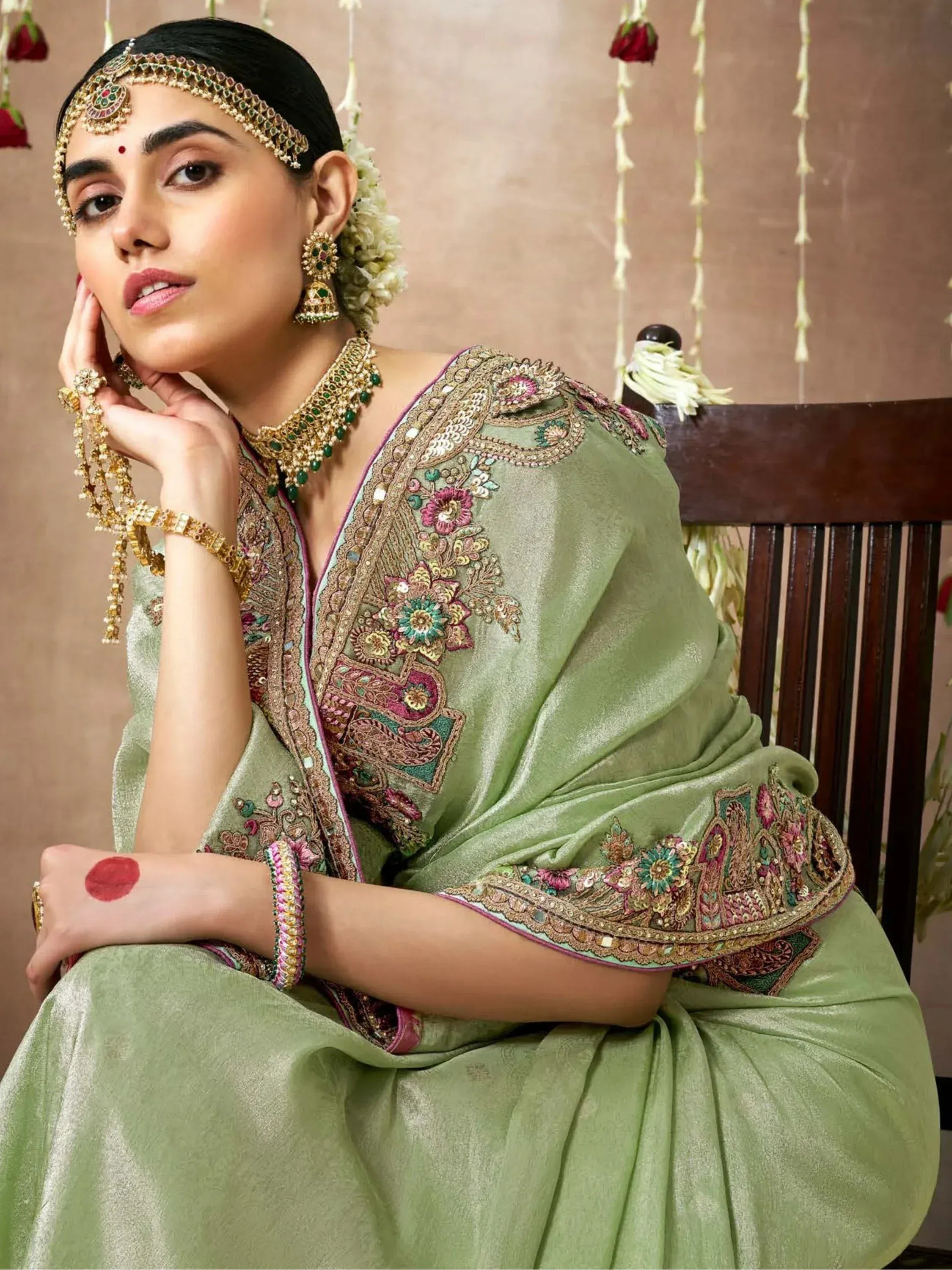 Woman in olive green embroidered Indian ethnic saree with gold jewelry and floral headpiece