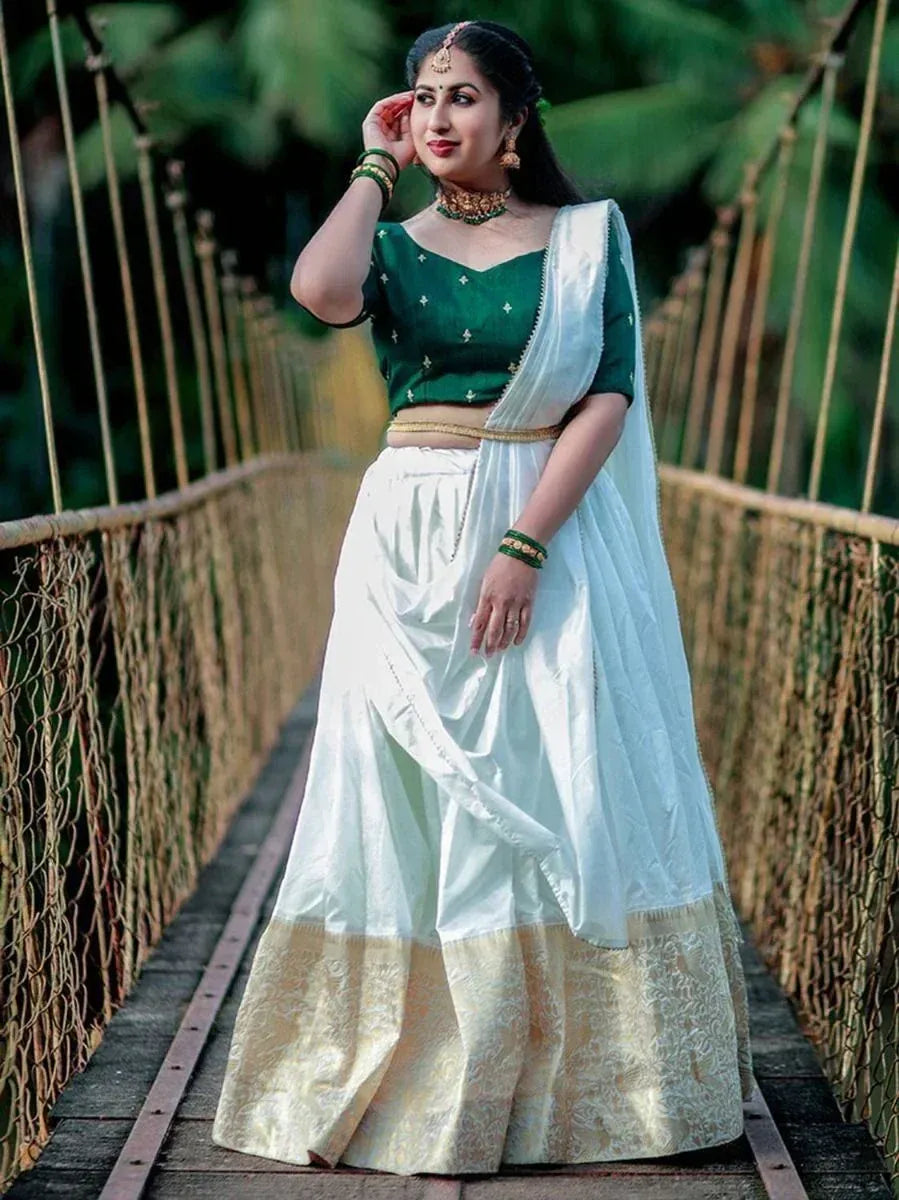 Woman in green embroidered blouse and white lehenga with gold border, standing on rustic bridge