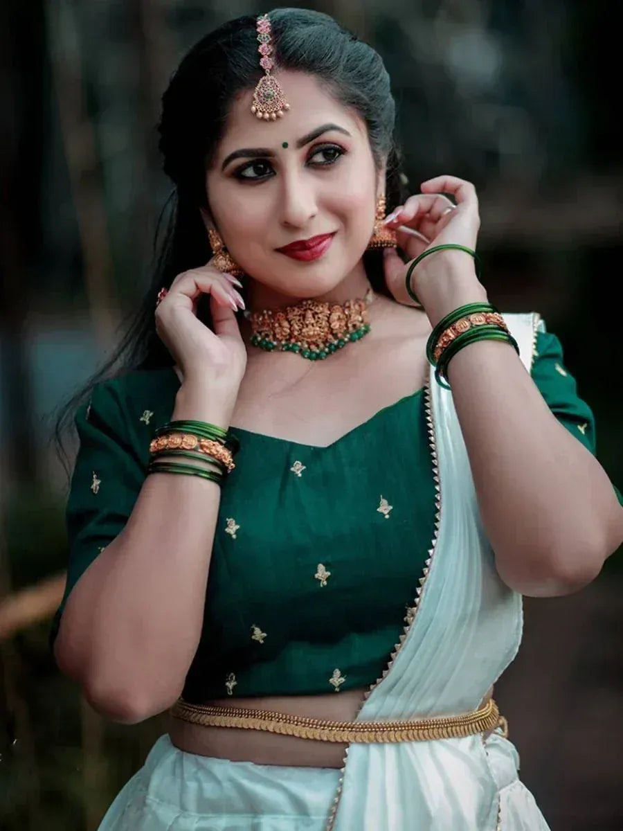 Woman in green embroidered blouse and white saree with gold jewelry, Indian ethnic wear