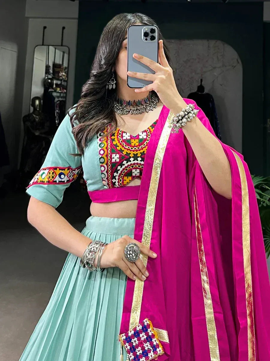 Woman in mint green lehenga choli with colorful embroidery and pink dupatta, styled with silver jewelry