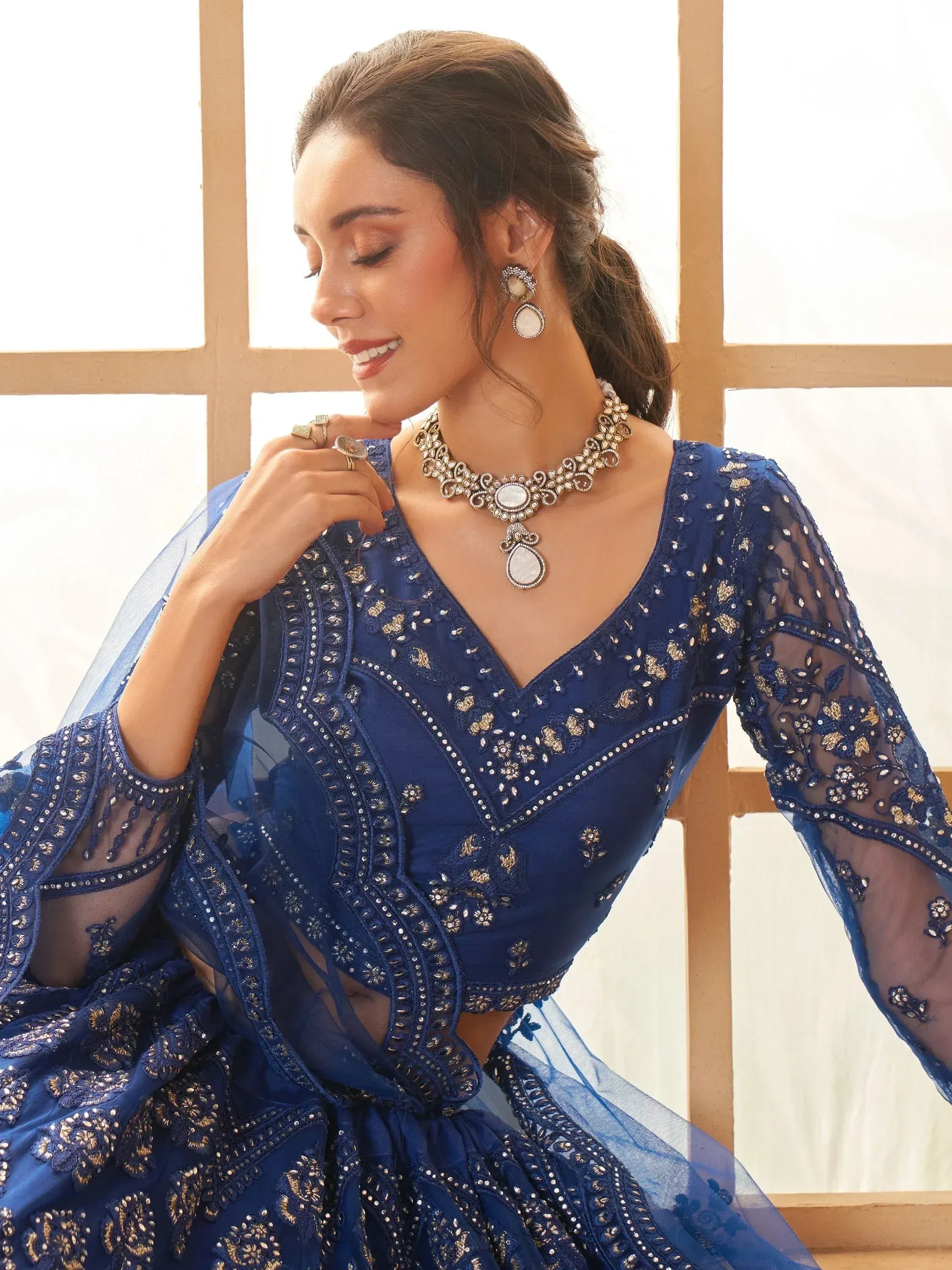 Elegant blue embroidered lehenga choli with sheer sleeves and gold detailing, paired with traditional jewelry.