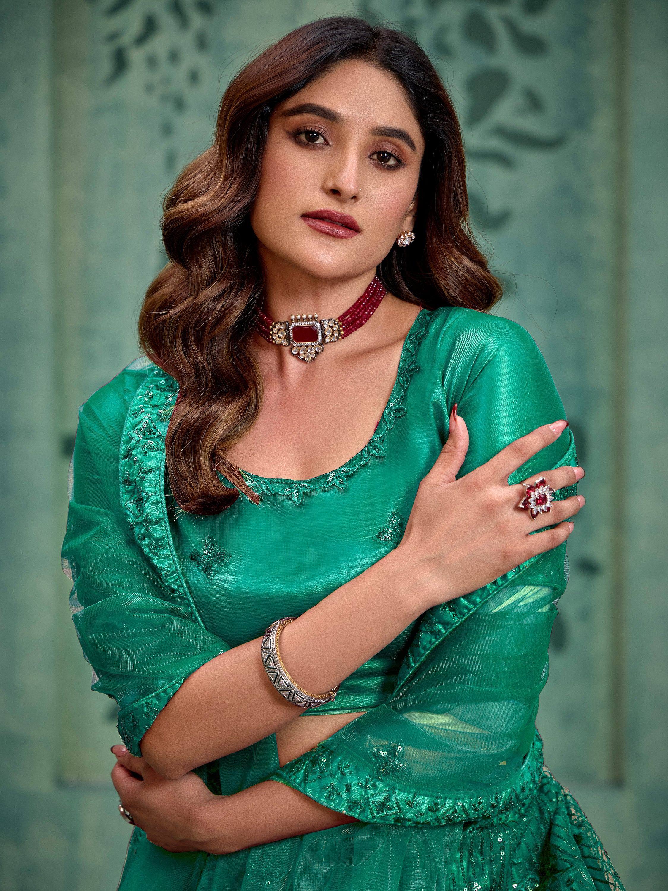 Emerald green ethnic gown with sequin detailing, paired with red gemstone jewelry for festive occasions.