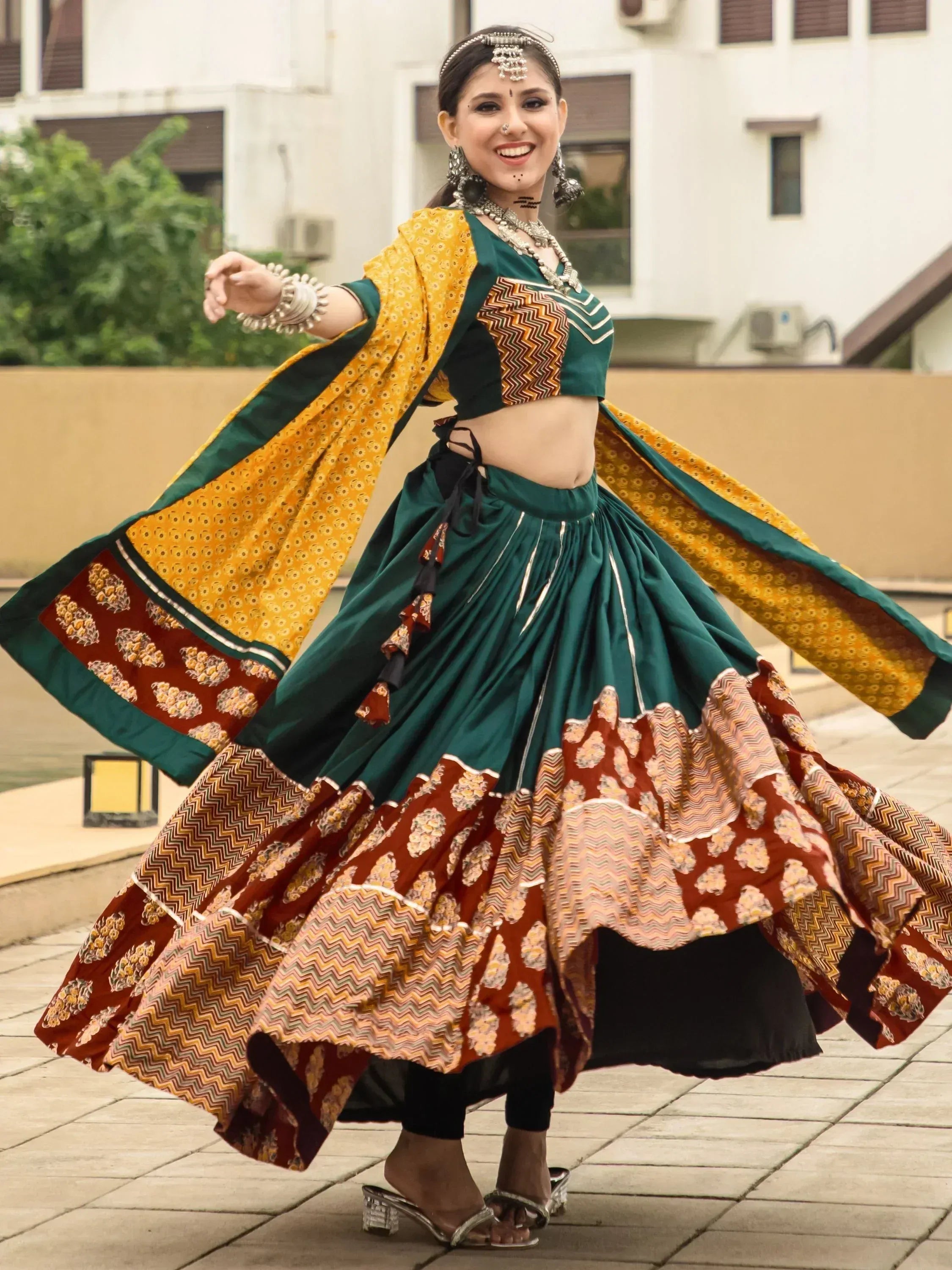 Woman in vibrant green and mustard Indian ethnic lehenga choli with printed dupatta, dancing outdoors.