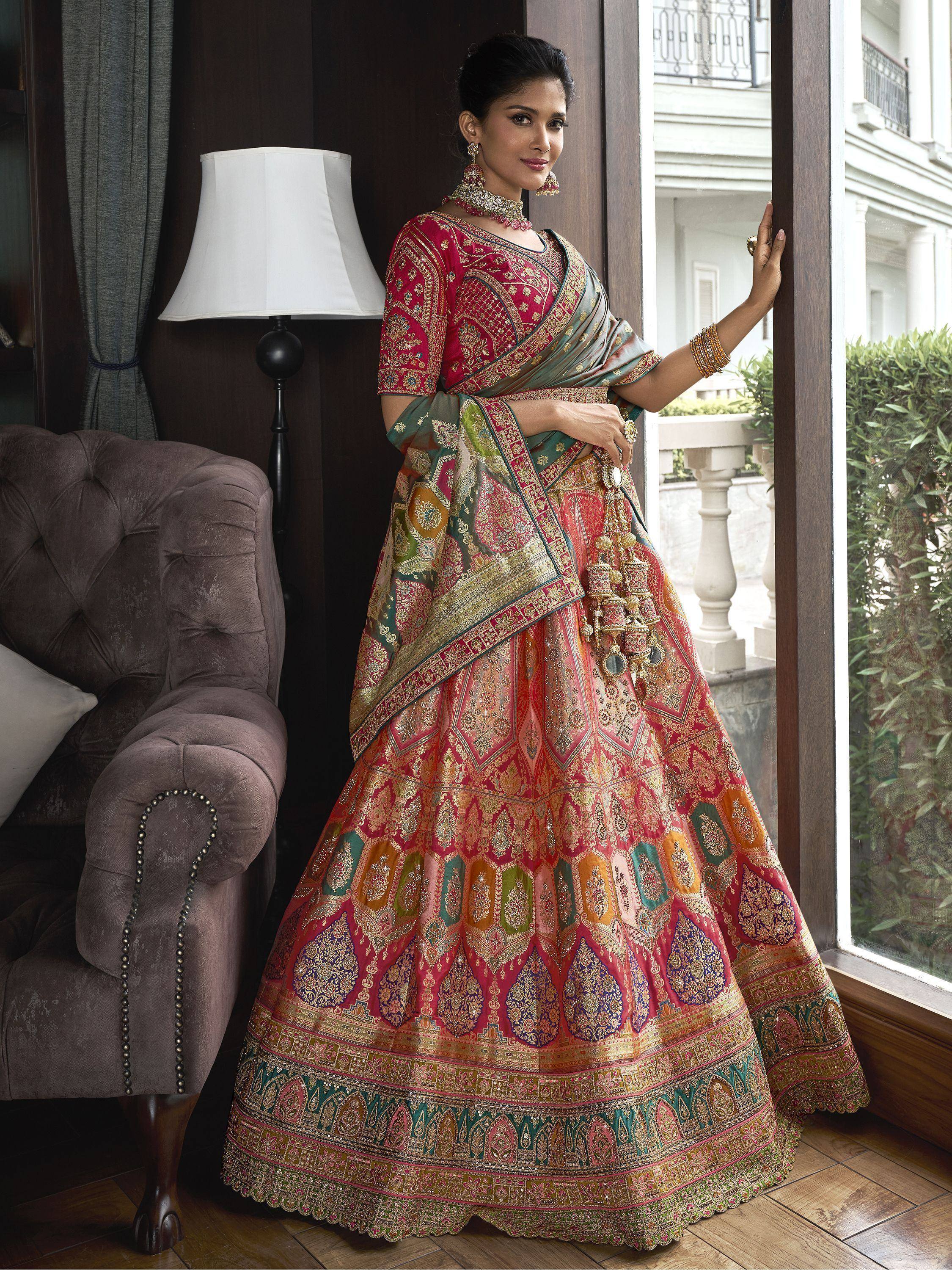 Woman in vibrant red and green designer lehenga choli with intricate embroidery, perfect for Indian ethnic wear occasions.