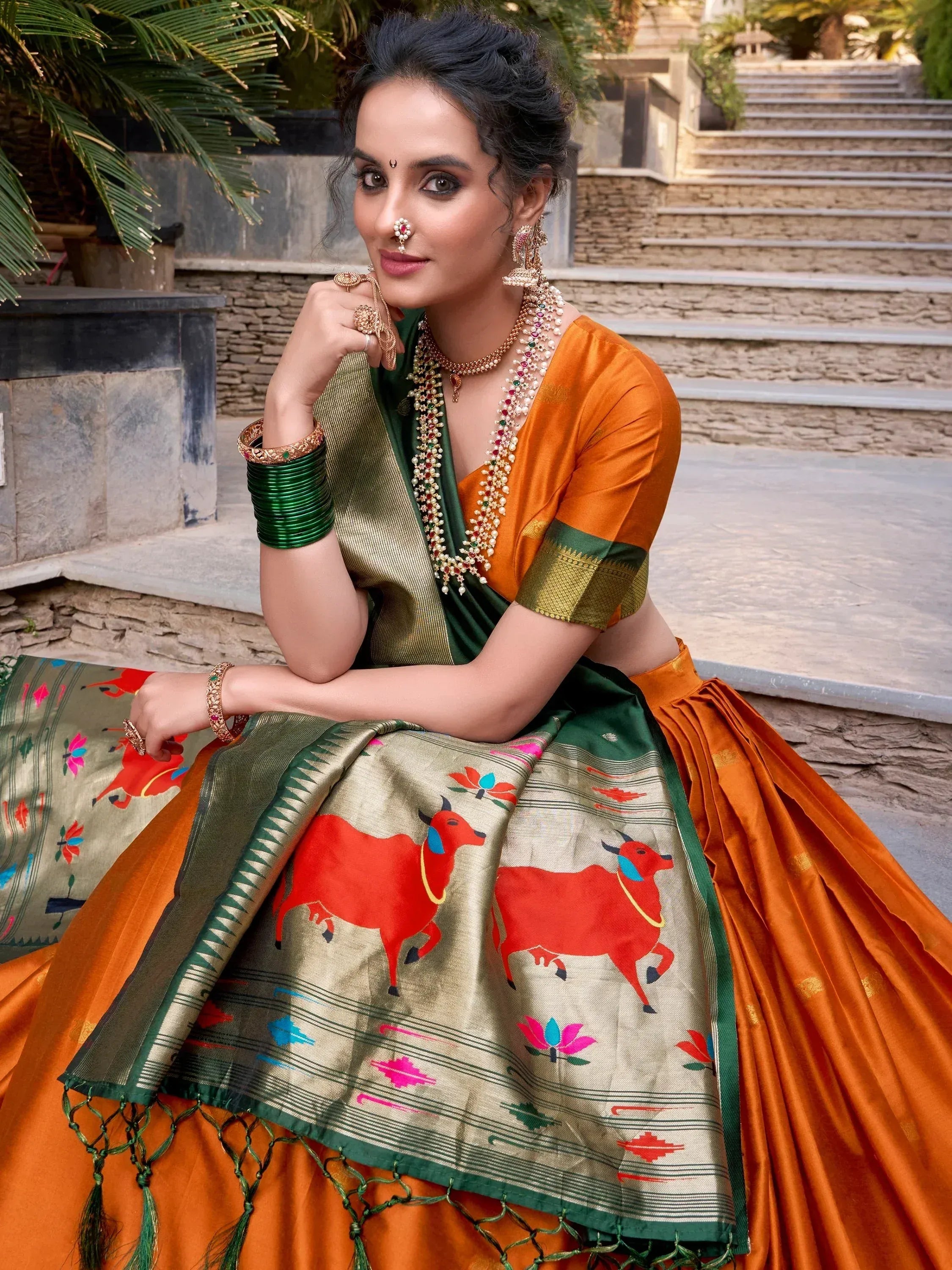 Woman in orange and green ethnic lehenga choli with cow print dupatta, traditional Indian jewelry