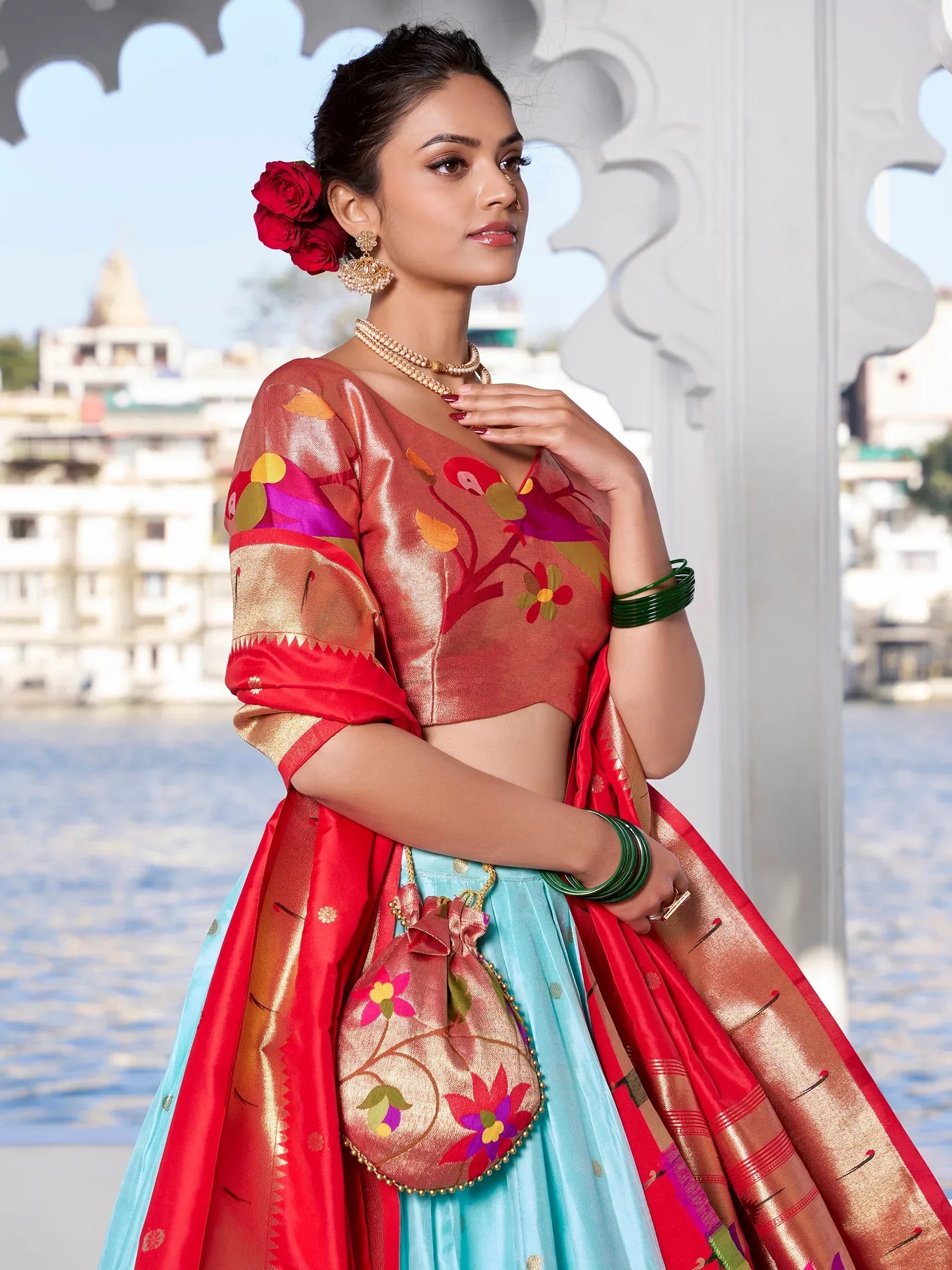 Woman in vibrant floral lehenga choli with red dupatta, green bangles, and temple backdrop
