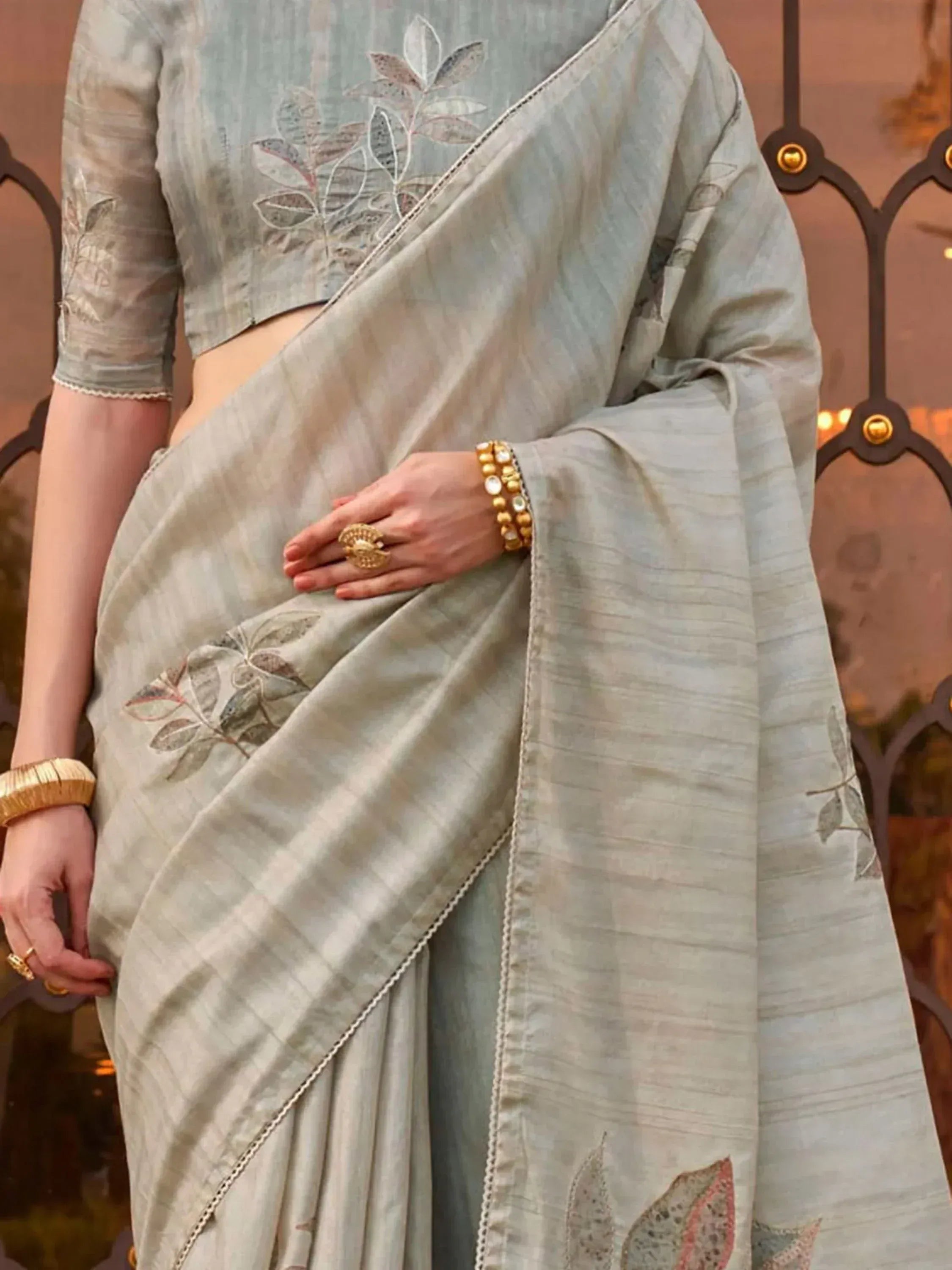 Elegant light grey saree with leaf embroidery, paired with matching blouse and gold jewelry for Indian ethnic wear.