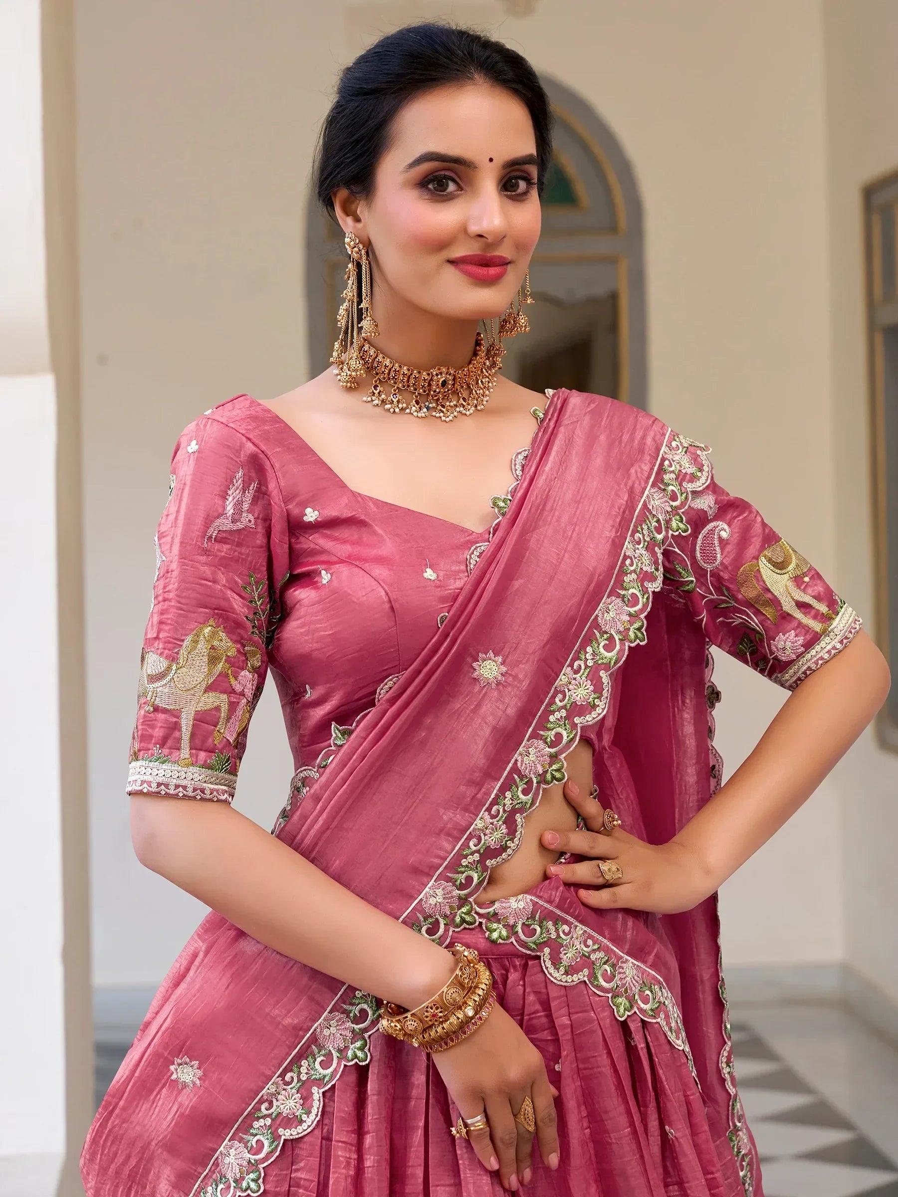 Pink embroidered lehenga choli with floral and horse motifs, paired with gold jewelry for Indian ethnic wear