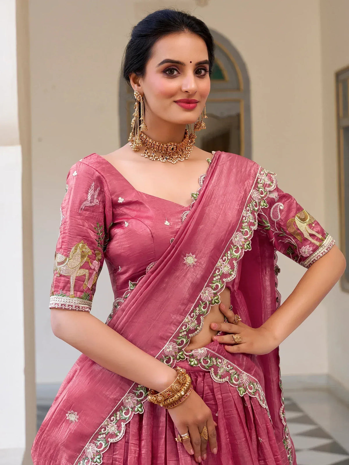 Pink embroidered lehenga choli with floral and horse motifs, paired with gold jewelry for Indian ethnic wear