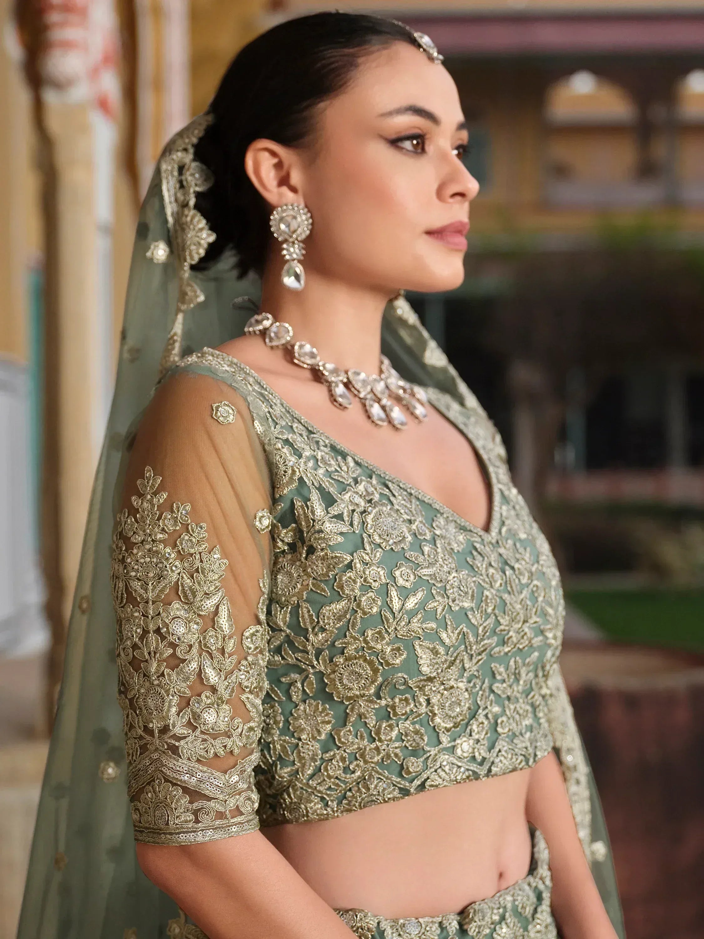 Elegant sage green lehenga choli with gold floral embroidery, sheer sleeves, and matching dupatta for Indian weddings.