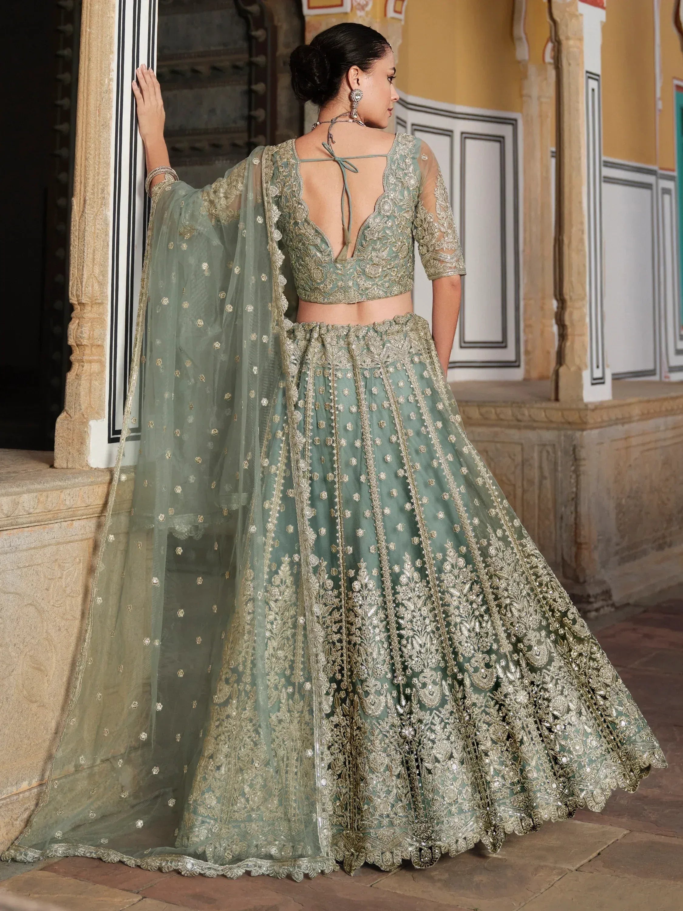 Elegant sage green lehenga choli with gold embroidery, sheer dupatta, and back tie blouse for Indian weddings.