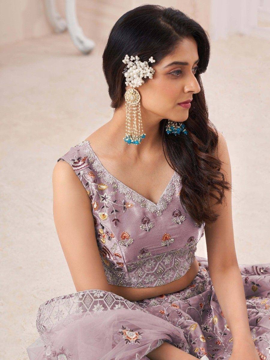 Woman in lavender embroidered lehenga choli with pearl hair accessory and blue jhumka earrings