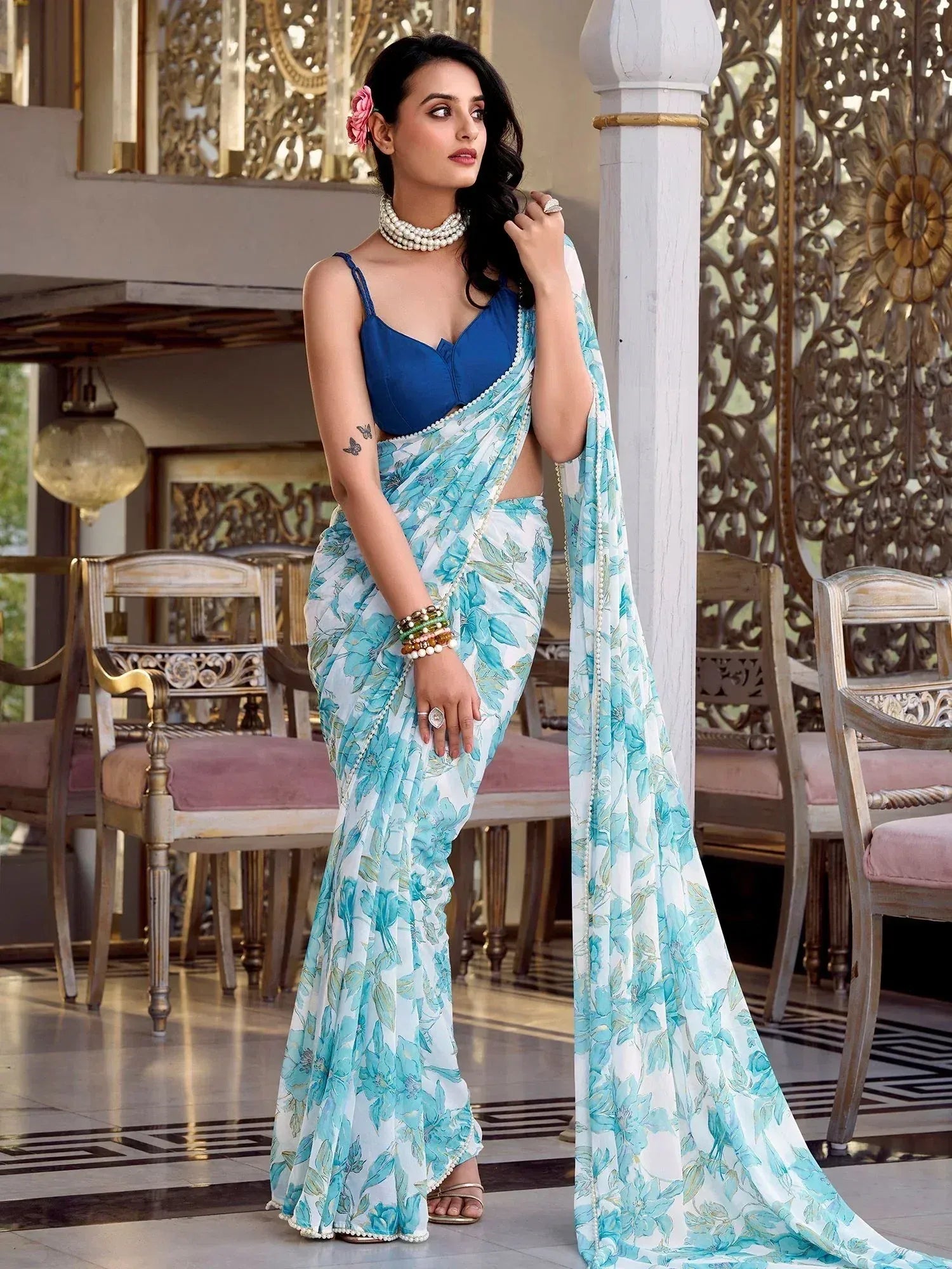 Woman in blue floral saree with pearl trim, styled with blue blouse and pearl jewelry, elegant ethnic wear