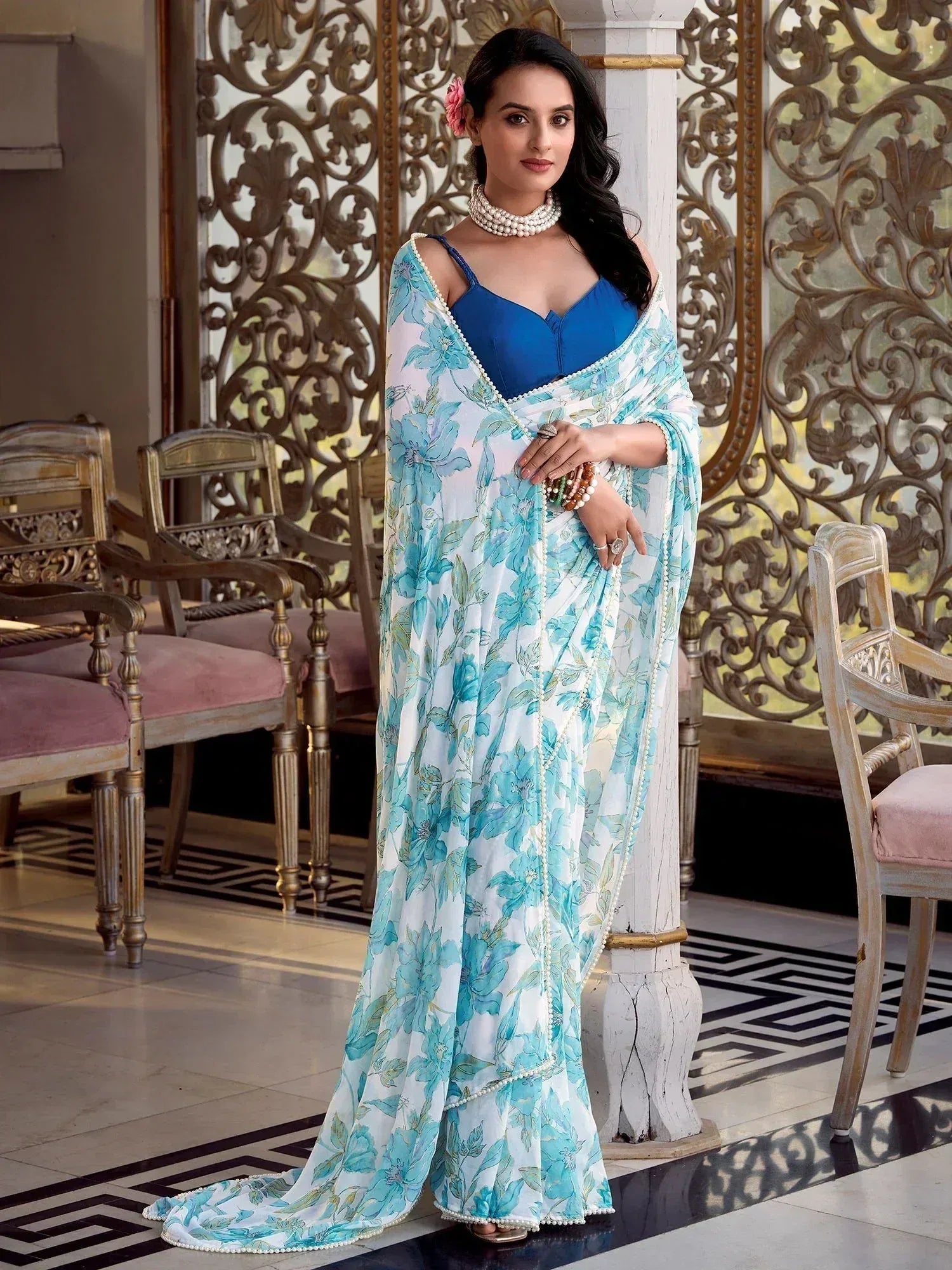 Woman in blue floral saree with pearl trim, styled with blue blouse and pearl jewelry for ethnic wear